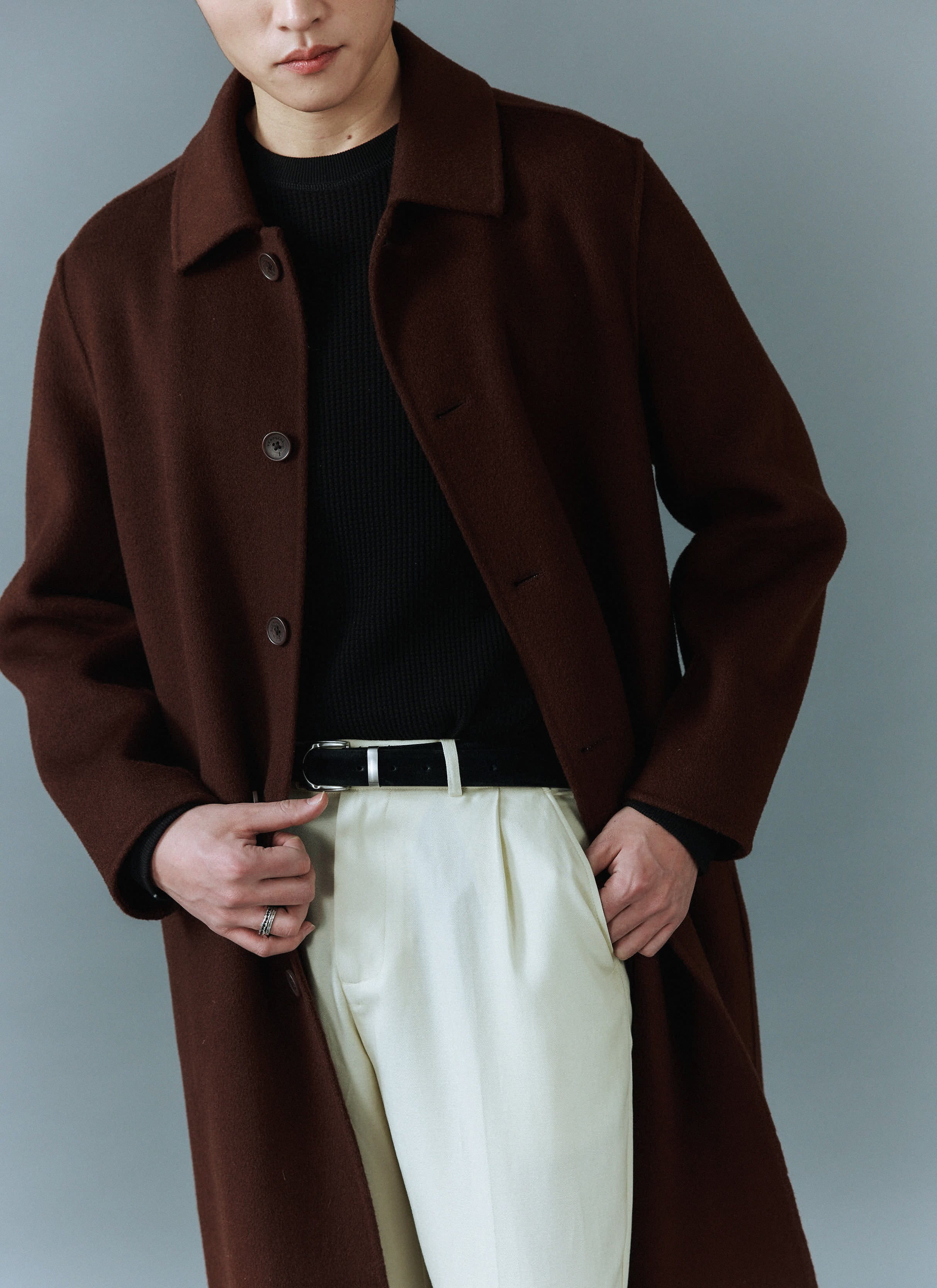A model wears the Percival Minnesota Overcoat in espresso wool over a black jumper and cream trousers.