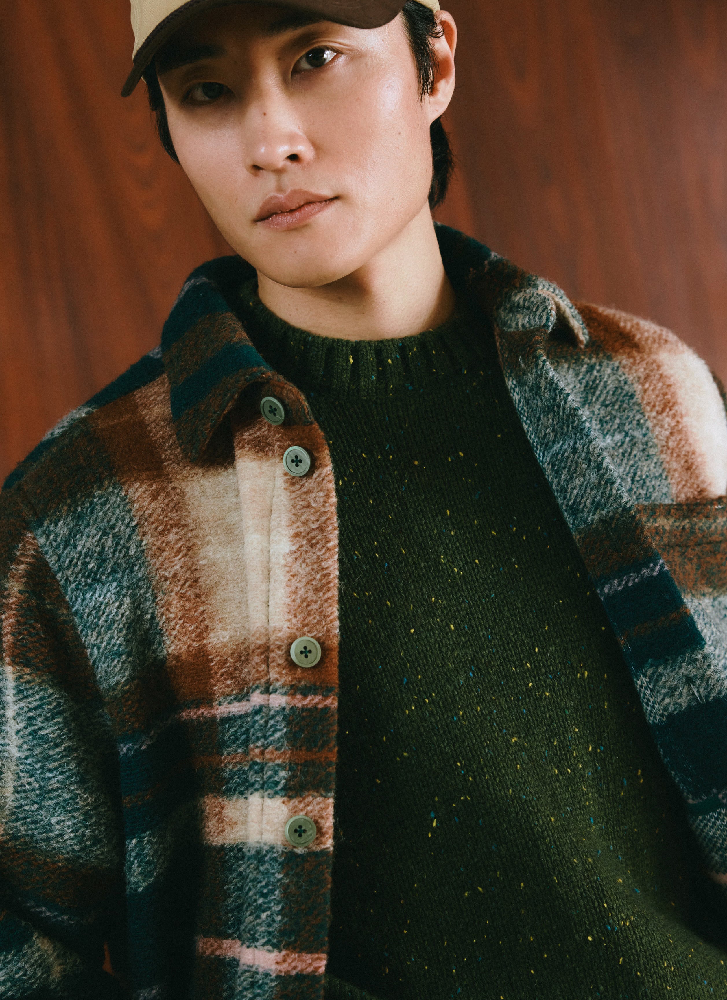 Close-up of a model wearing the Percival multi check wool Knowles overshirt layered over a green knit.