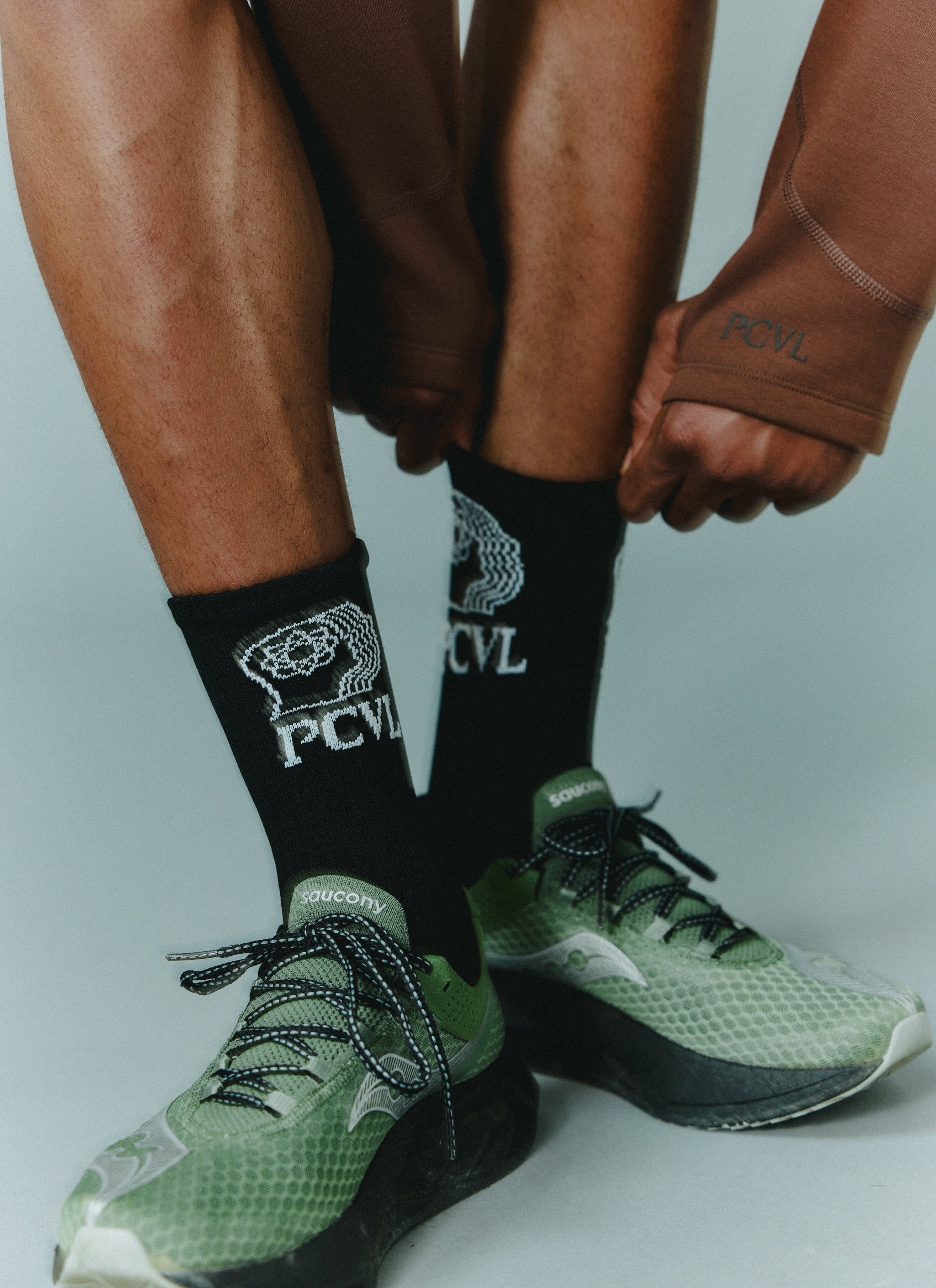 A detailed shot of a model wearing the black PCVL jacquard graphic sport socks from Percival with green trainers.