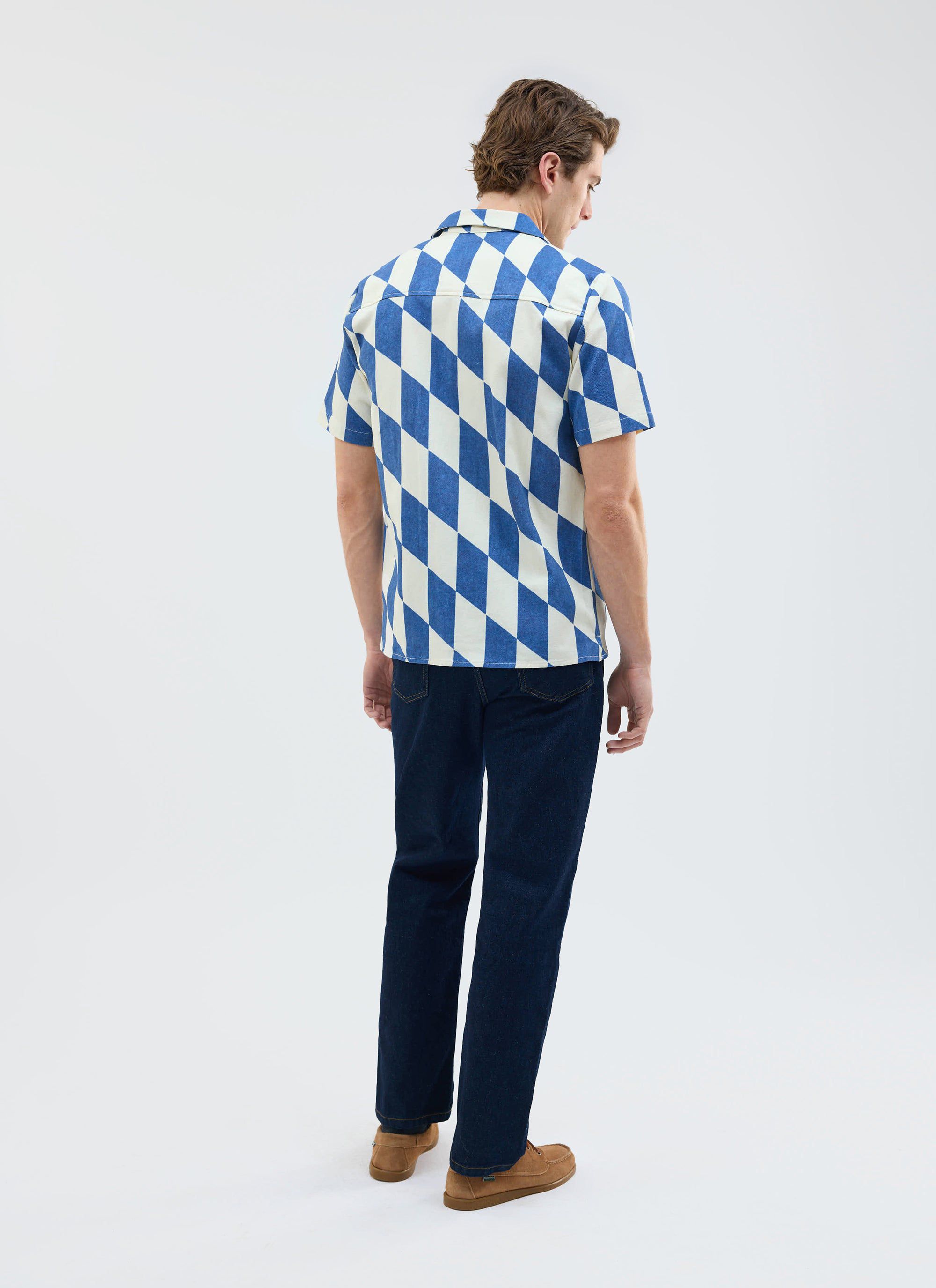 Back view of a model wearing the ecru and navy diamond print Market Cuban Shirt from Percival with dark jeans.
