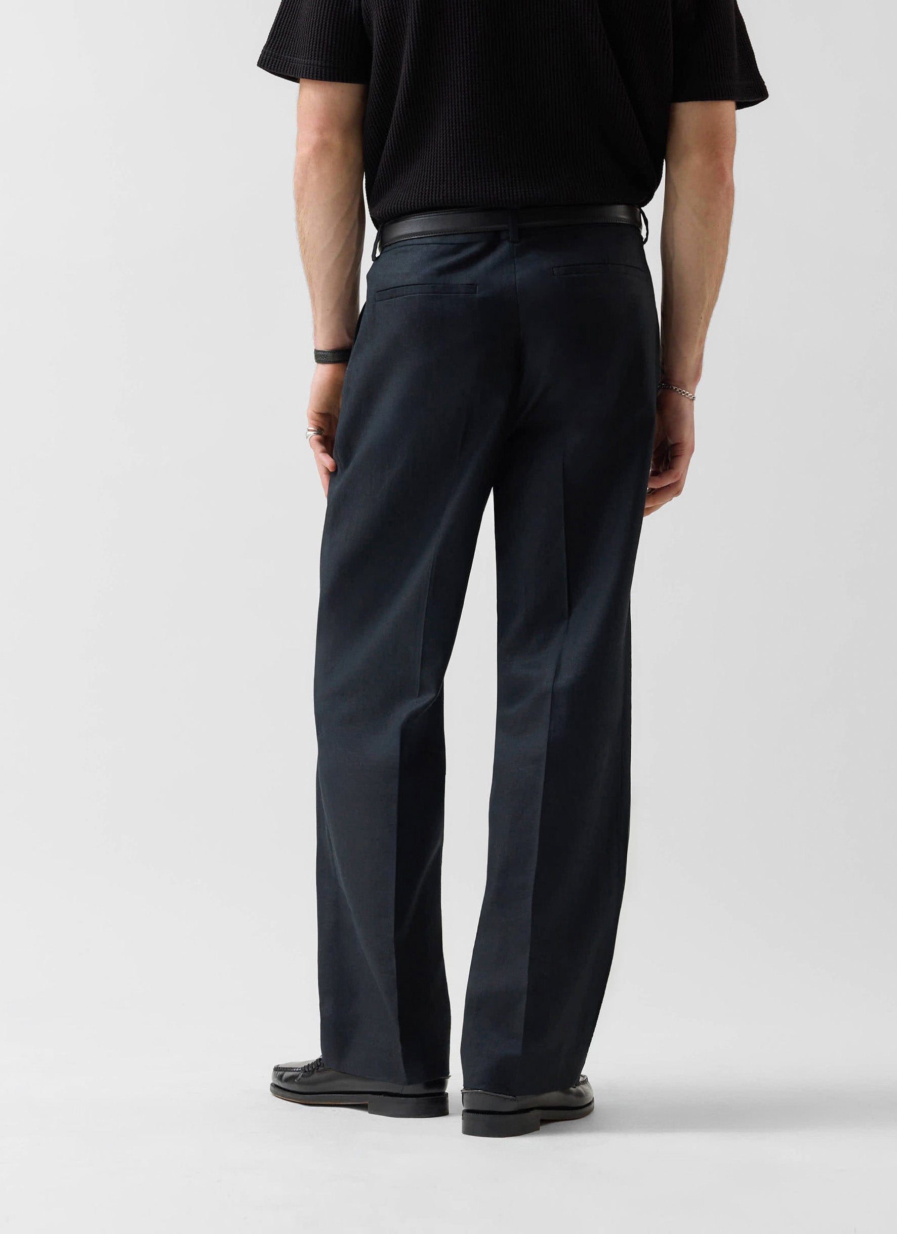A model viewed from behind wearing the Percival Wide Leg Trousers in black linen, showing off the relaxed, straight fit.