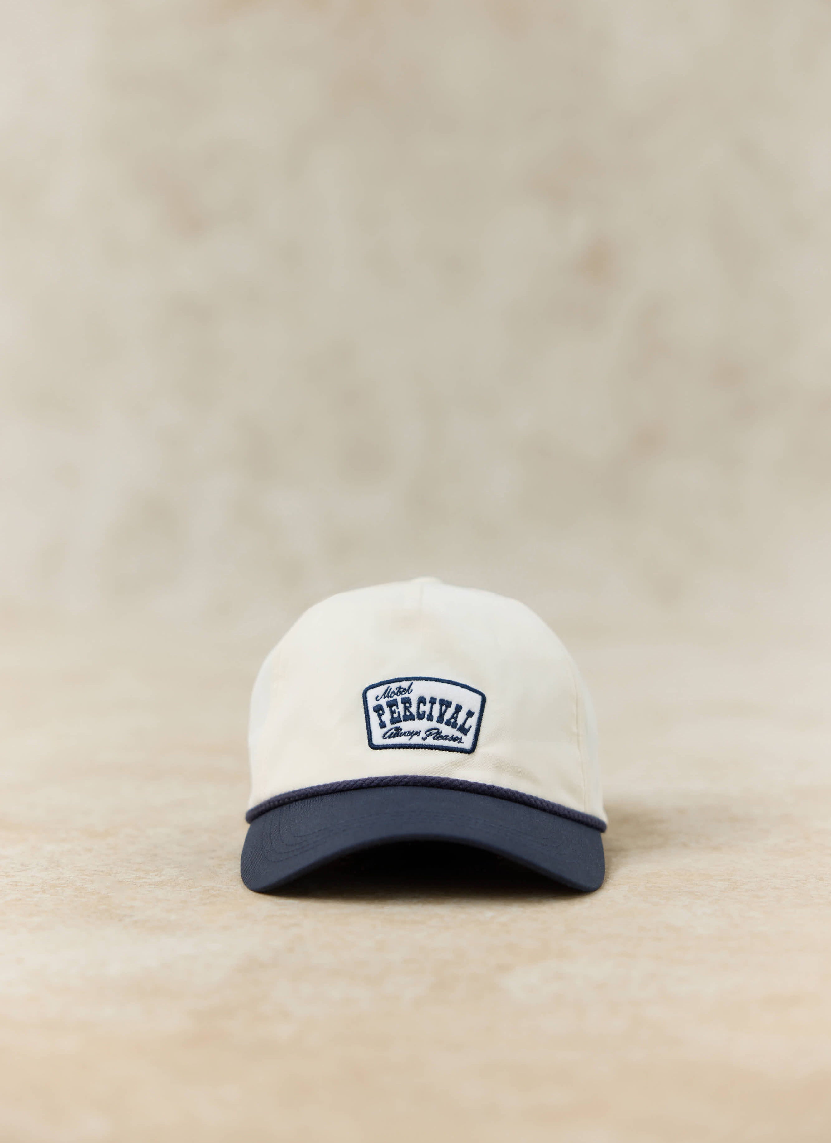 Percival Donovan soft trucker cap in cream with a contrast navy peak and motel-inspired embroidered patch.