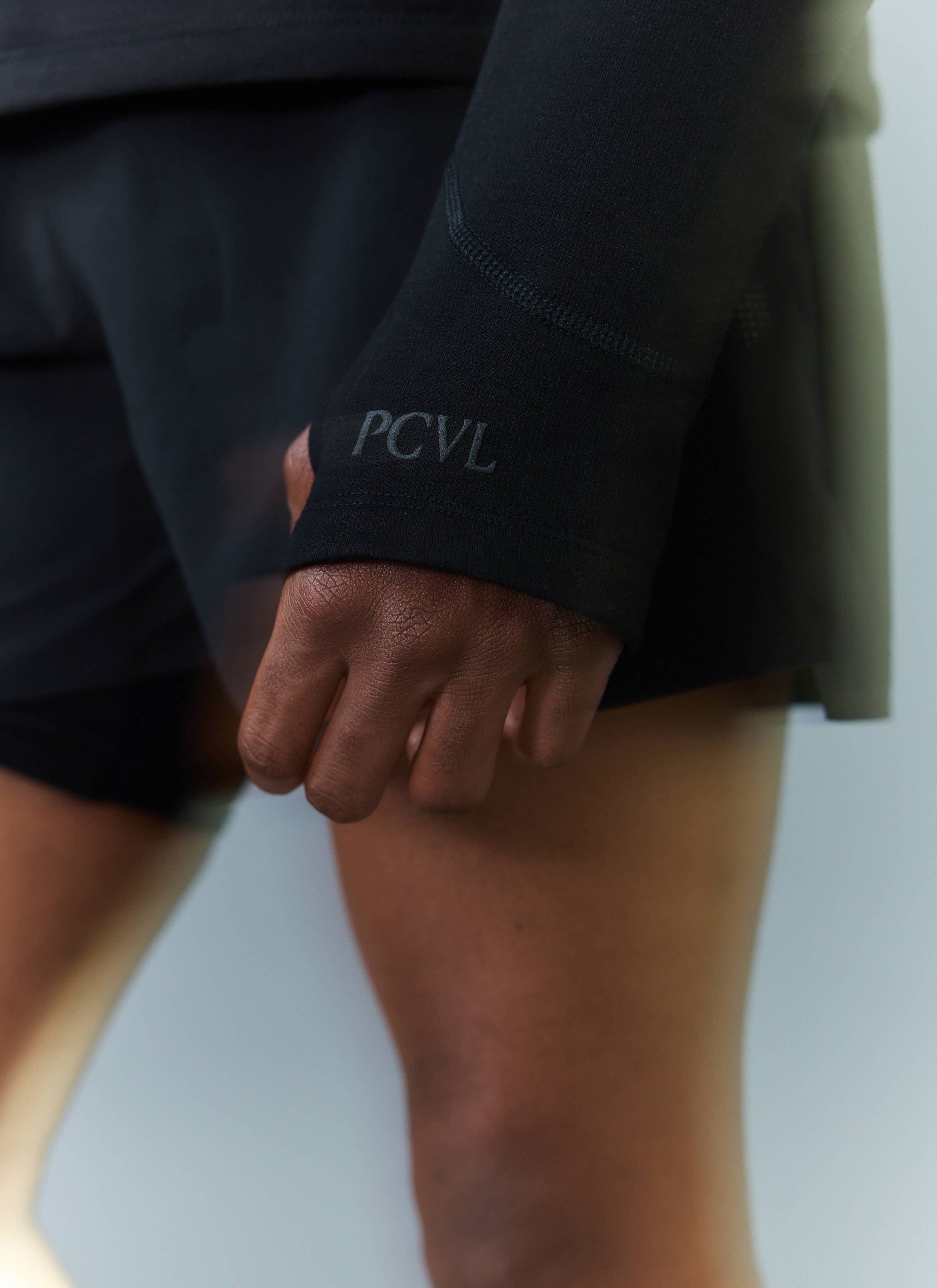 A close-up of the cuff on the black PCVL Base Layer Quarter Zip by Percival, showing the thumbhole and tonal logo detail.