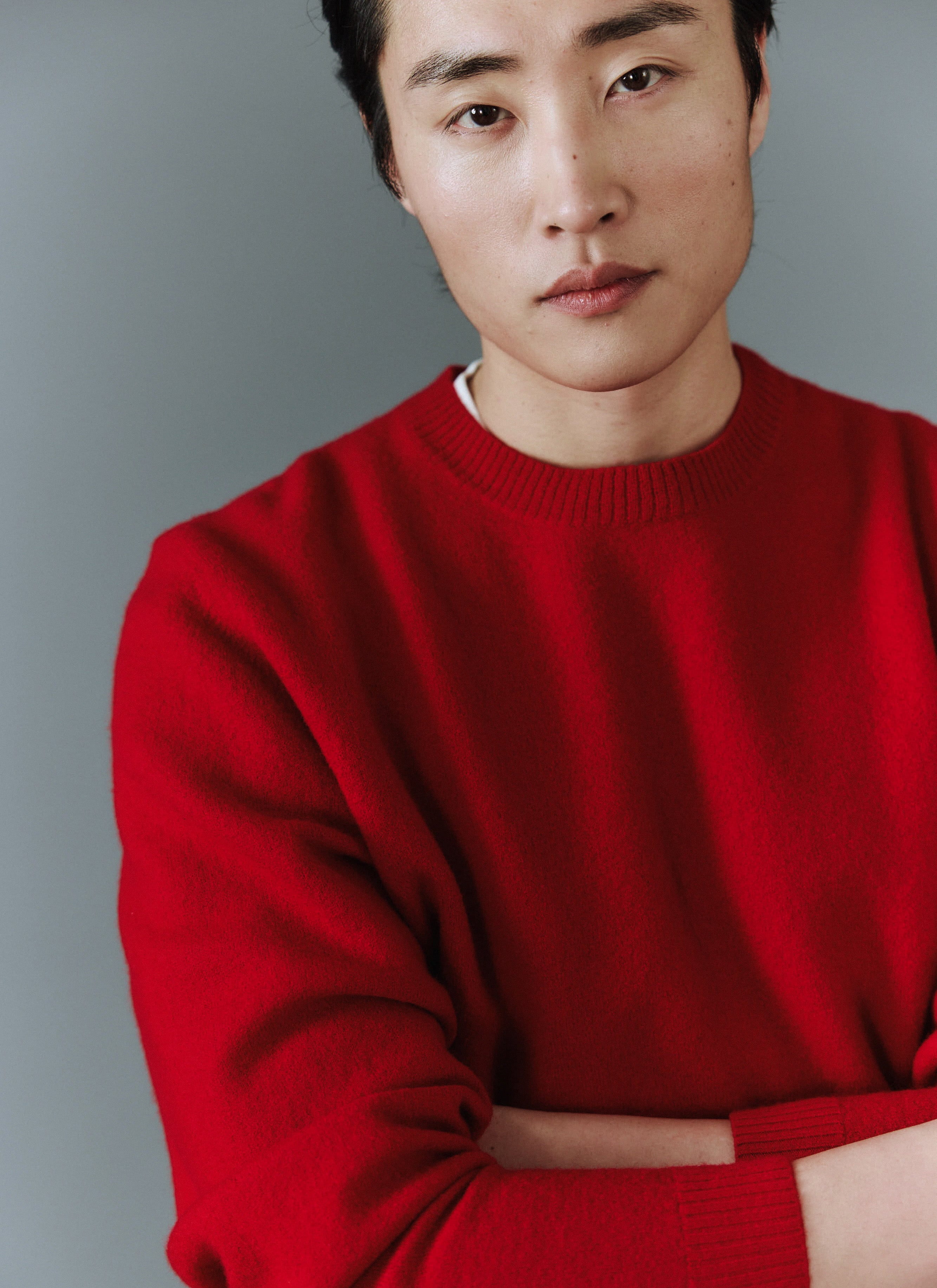 A close-up of a model wearing the red Felted Regular Jumper in merino wool by Percival against a grey background.