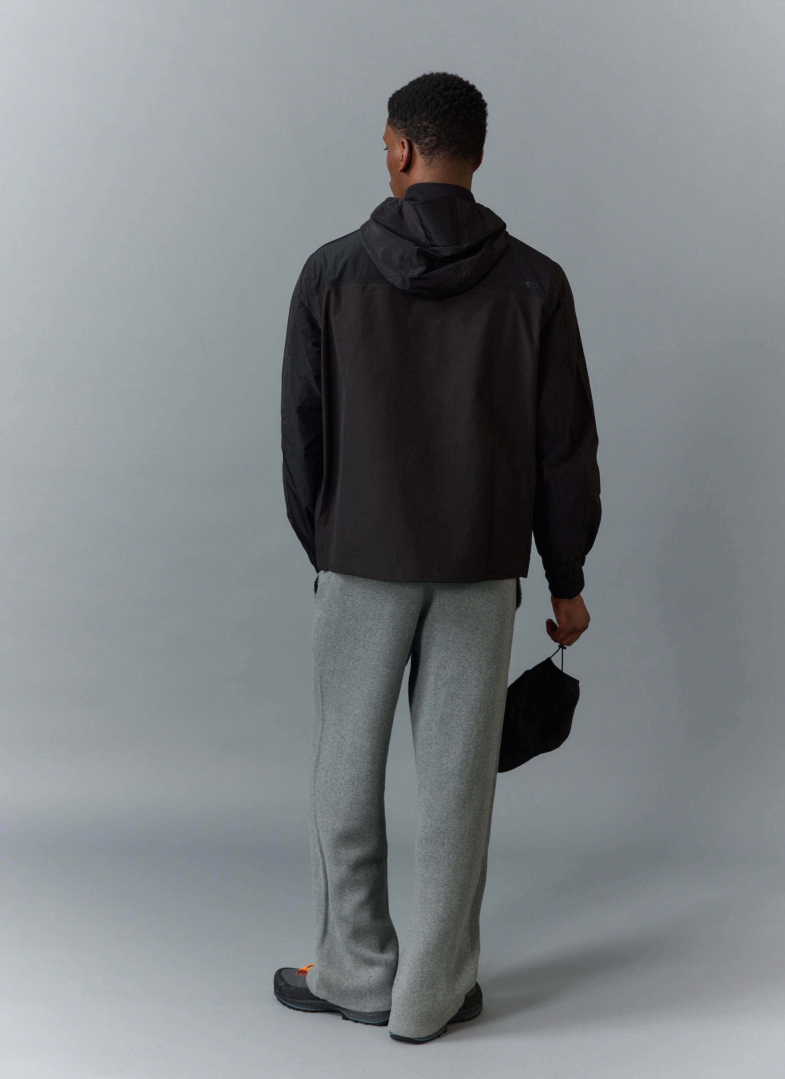Back view of a model wearing the black PCVL Zip Through Water Resistant Jacket from Percival, styled with grey trousers.