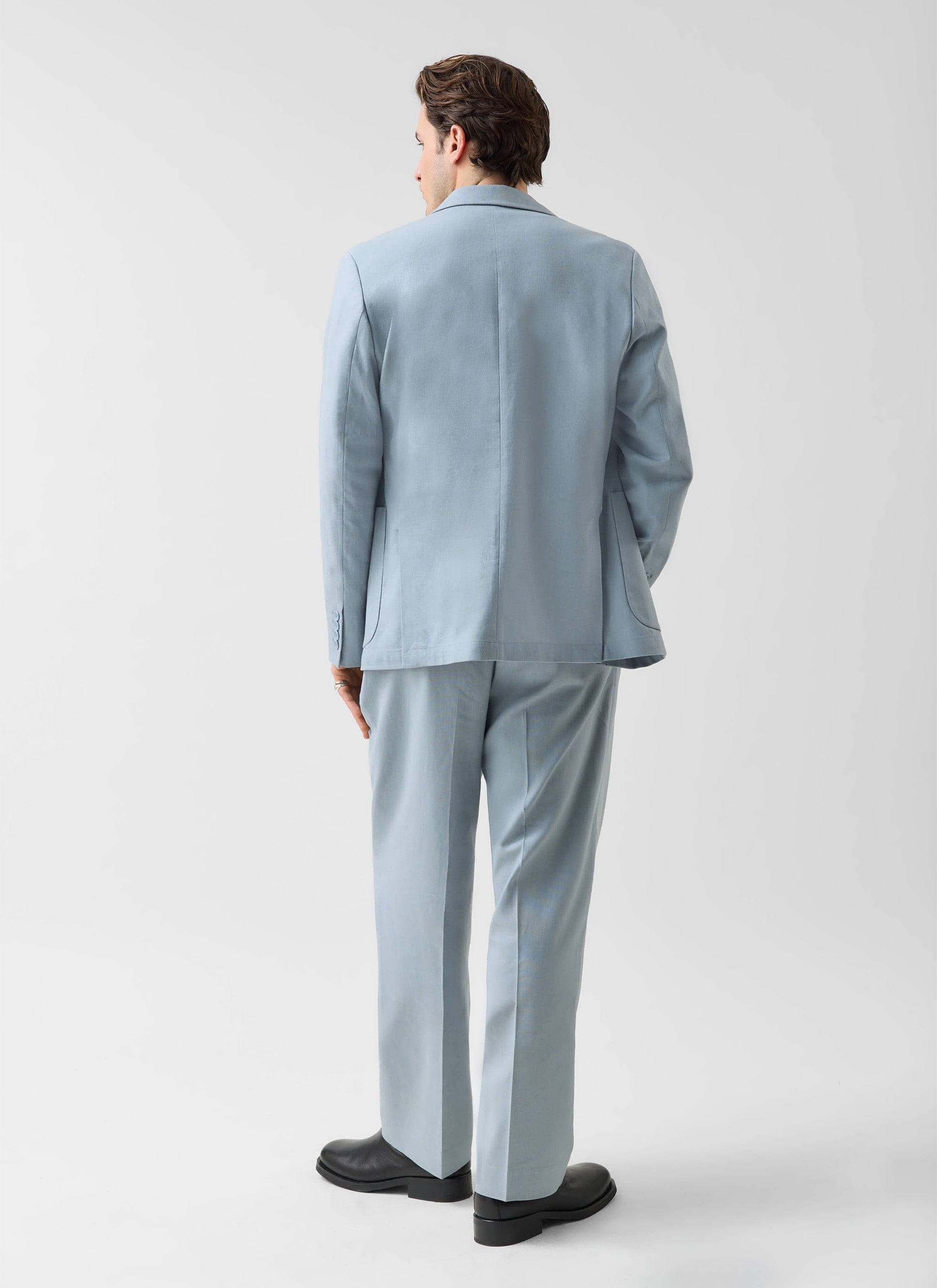 A model, seen from behind, wears the Percival Tailored Linen Blazer and matching trousers in light blue.