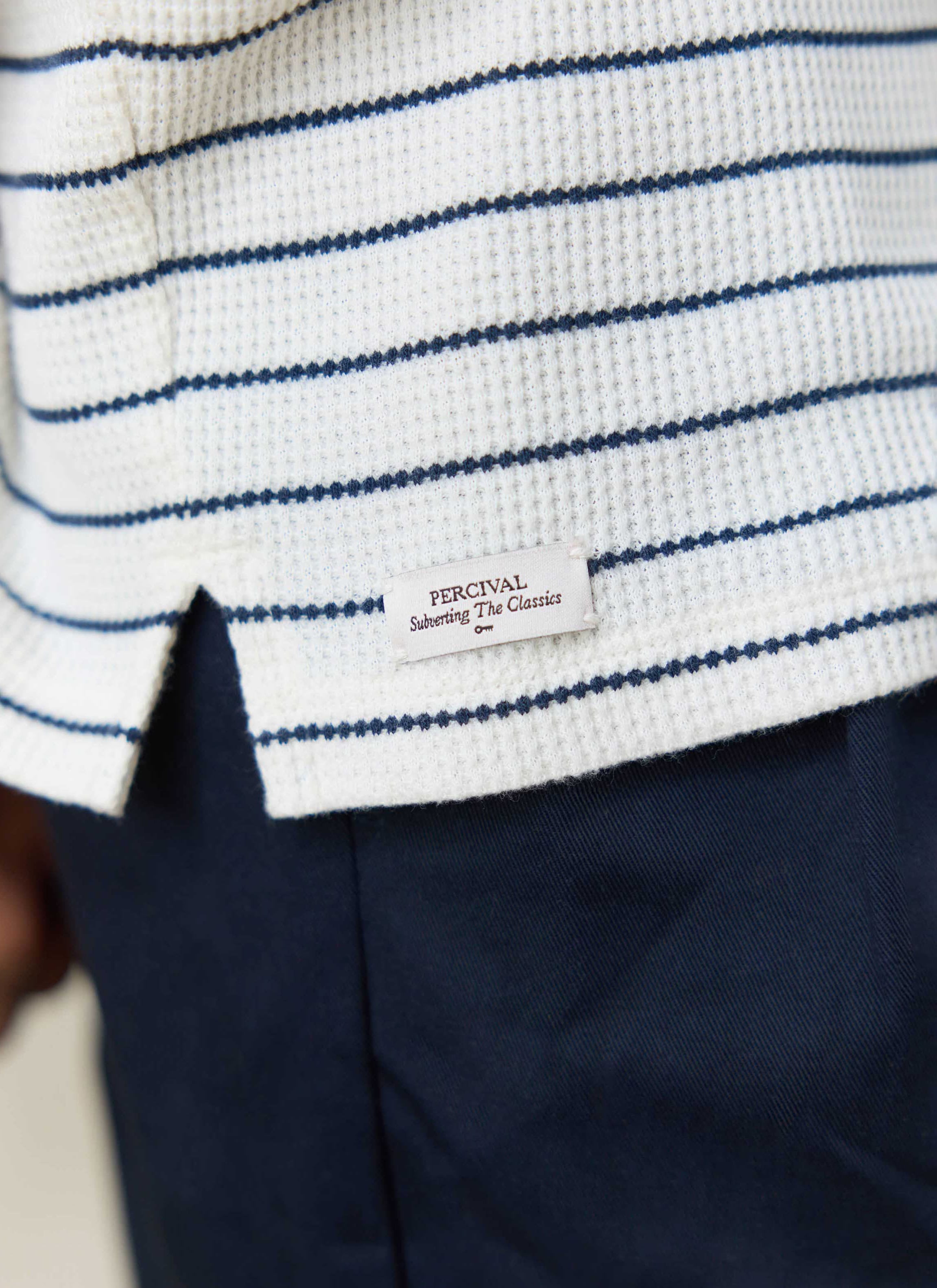 Close-up of the cream and navy striped organic cotton waffle texture and branded side split label by Percival.