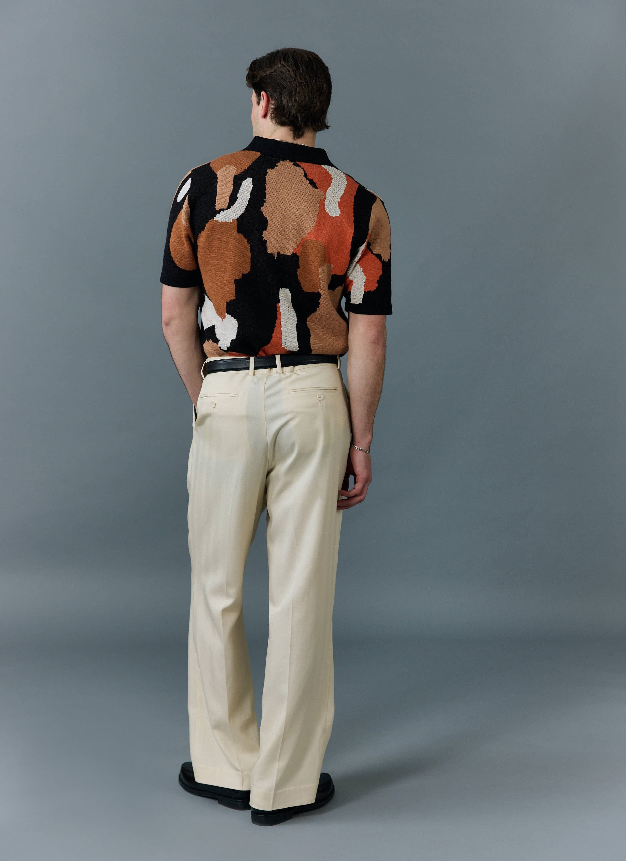 A man photographed from behind wearing the Percival Impressionist Jacquard knitted shirt with cream trousers.