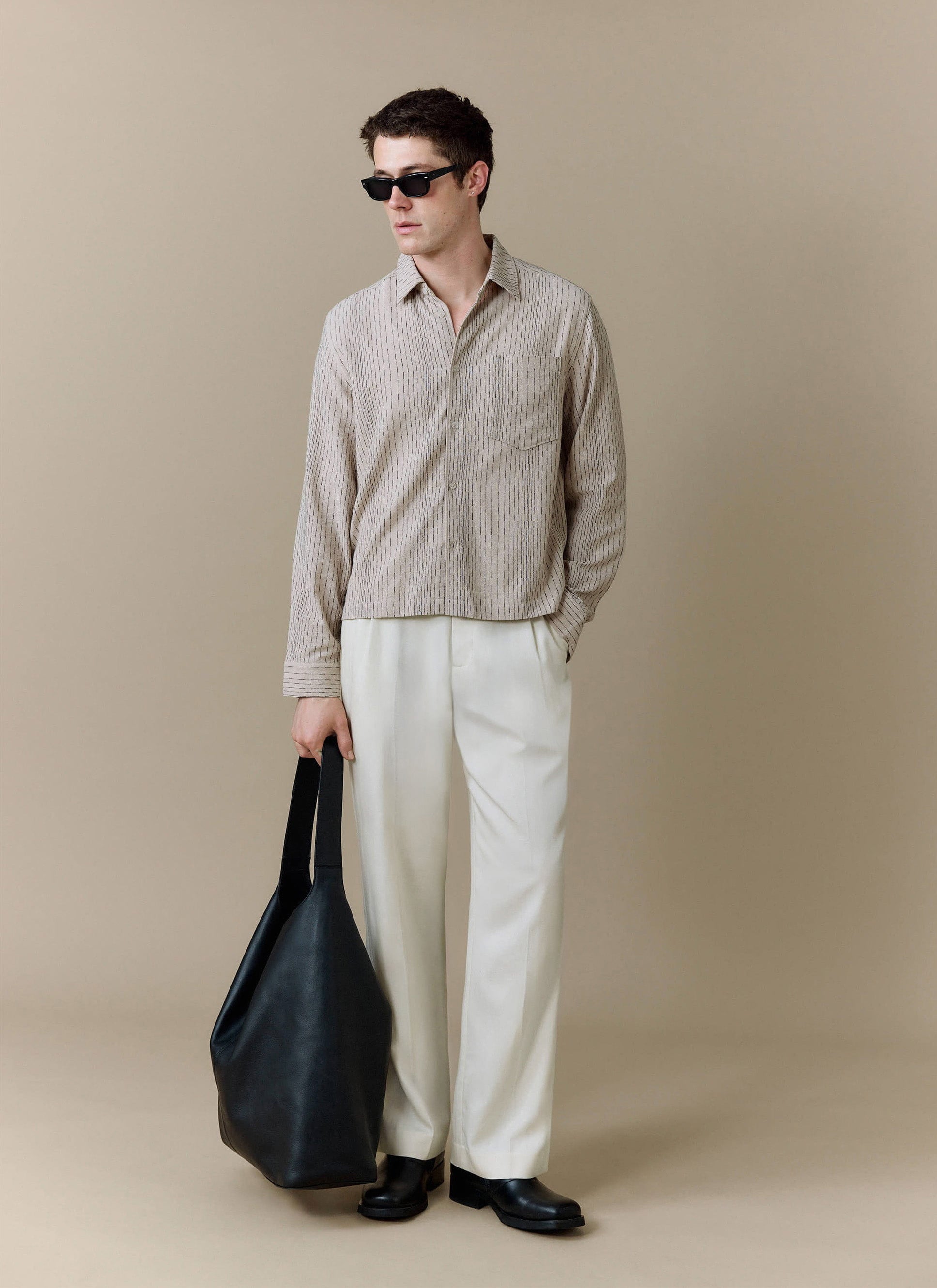 A model wears the Percival Leland Cuban Boxy Shirt in ecru, styled with white trousers, sunglasses and a black tote bag.