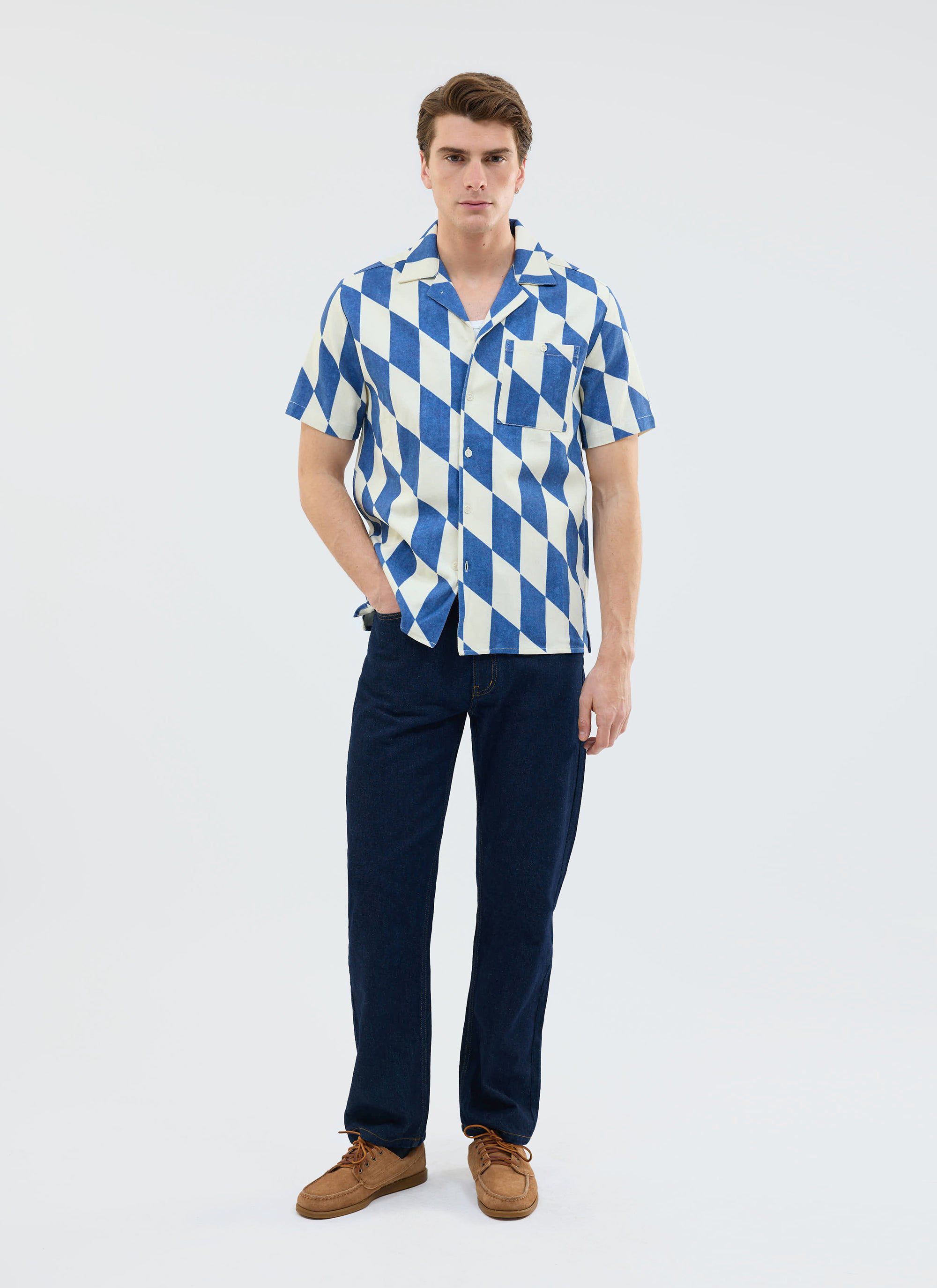Model wears the Percival Market Diamond Cuban Shirt in ecru and navy, styled with dark jeans and brown shoes.