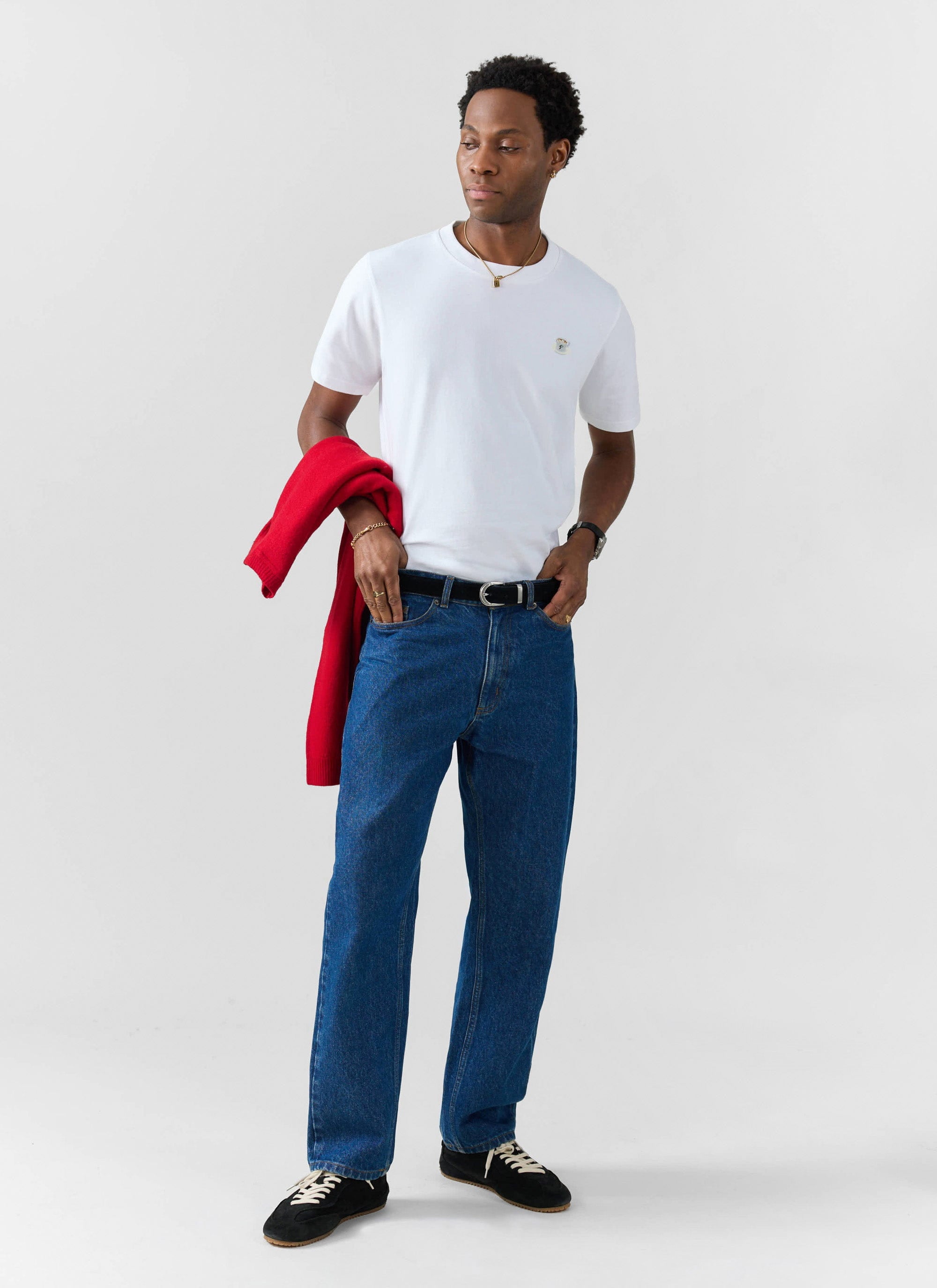 A model wears the white organic cotton Latte Embroidered T Shirt from Percival, styled with blue jeans and a red jumper.