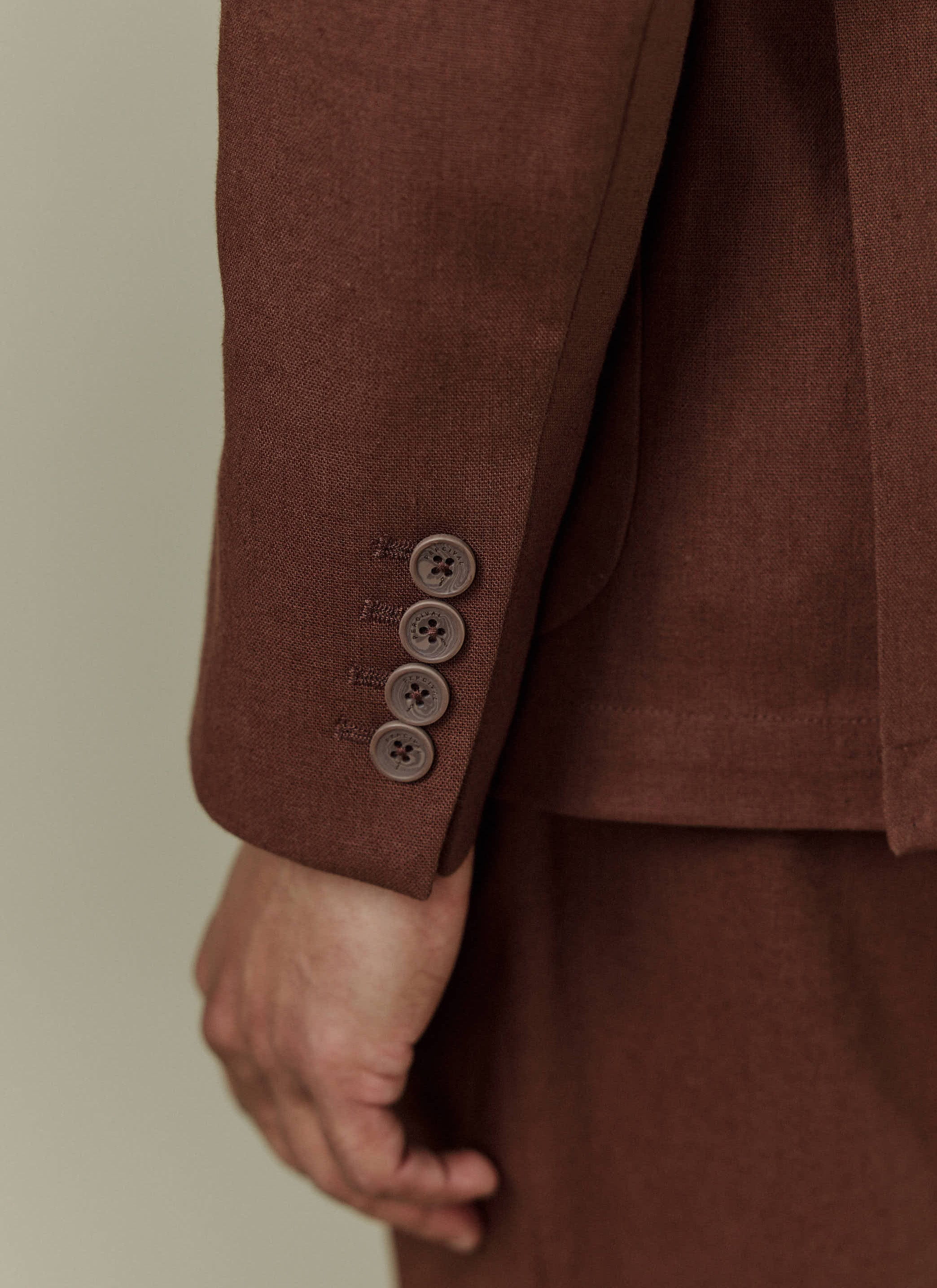 A close-up of the cuff of the brown Tailored Linen Blazer, showing the four Percival branded buttons.