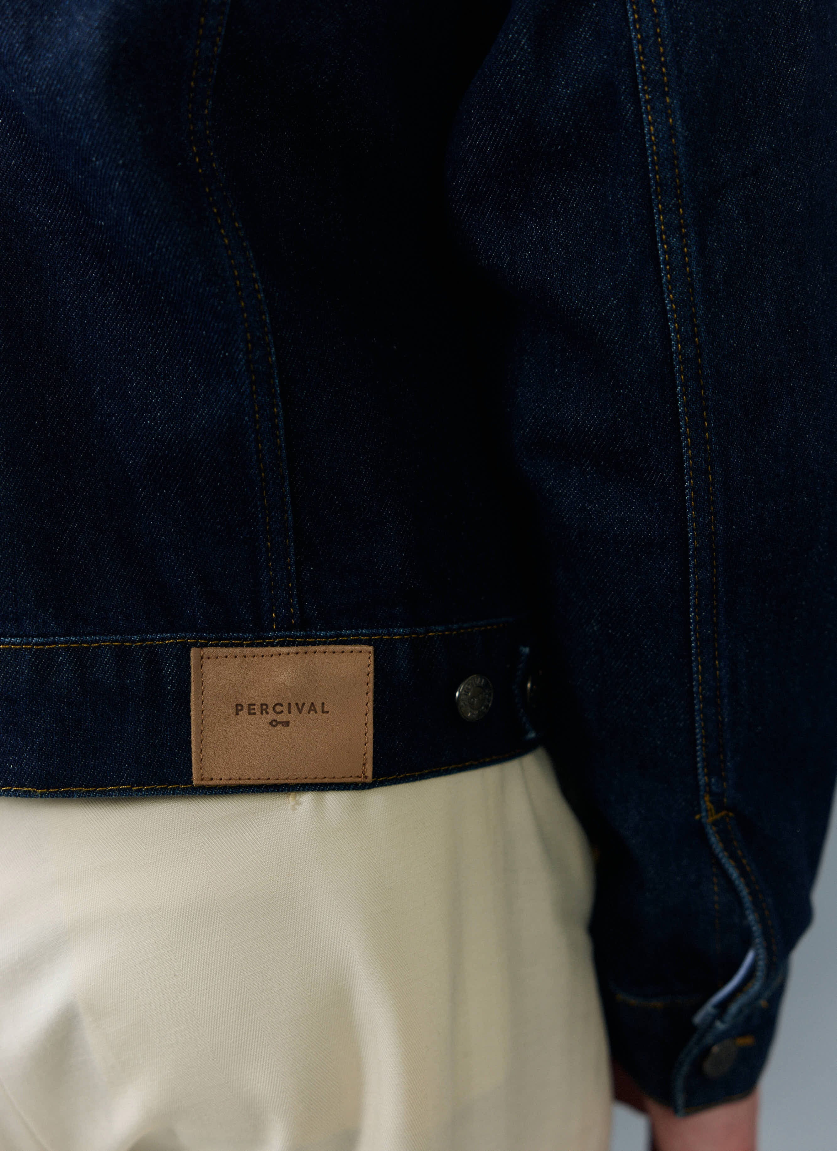 Close-up of a model wearing the Percival Western Trucker Jacket, showing the branded leather patch on the dark indigo denim.