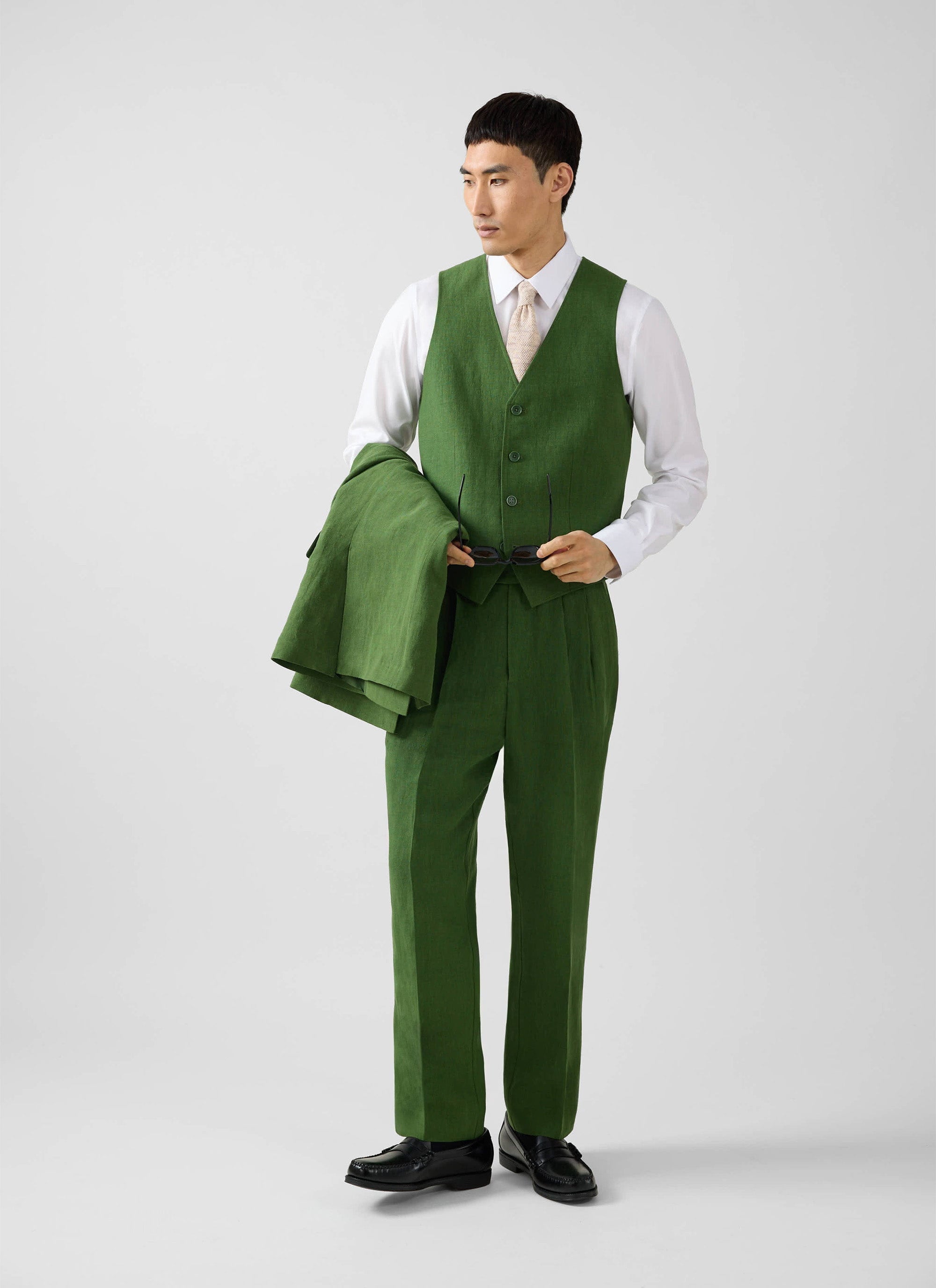 A model wears the Percival Linen Waistcoat in forest green as part of a three-piece suit in a studio setting.