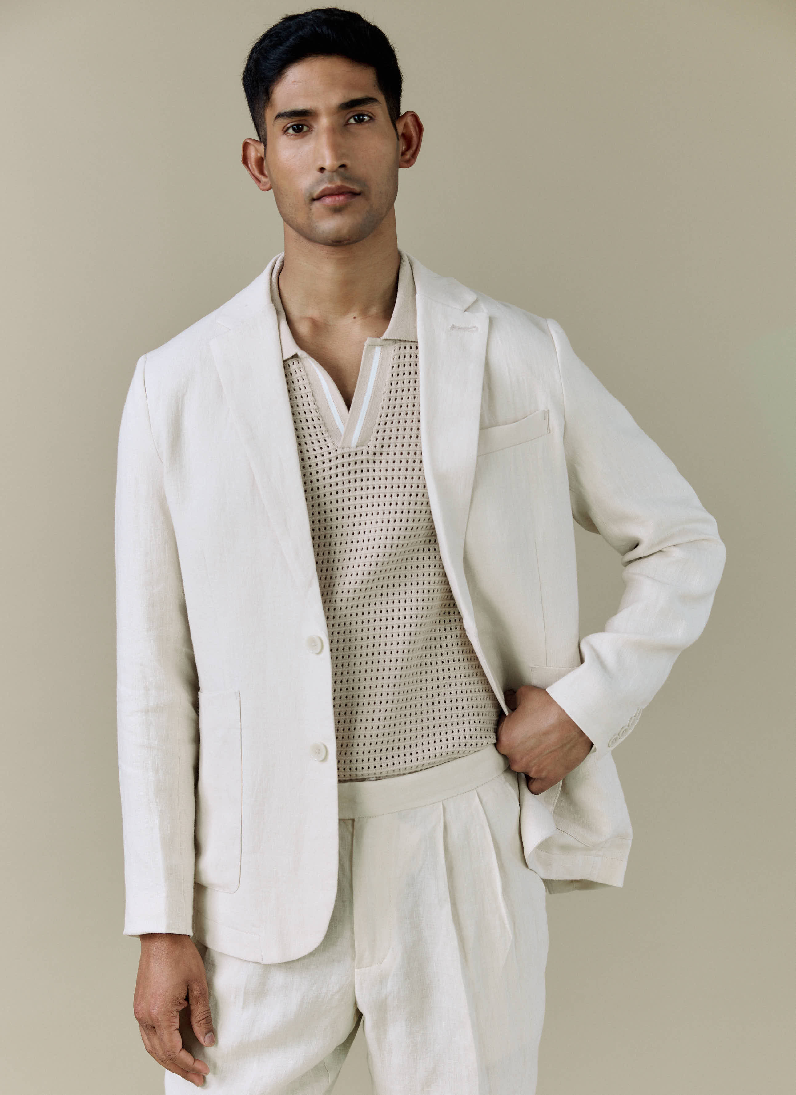 A model wears the Percival Tailored Linen Blazer in cream, styled with a knitted polo shirt and matching linen trousers.
