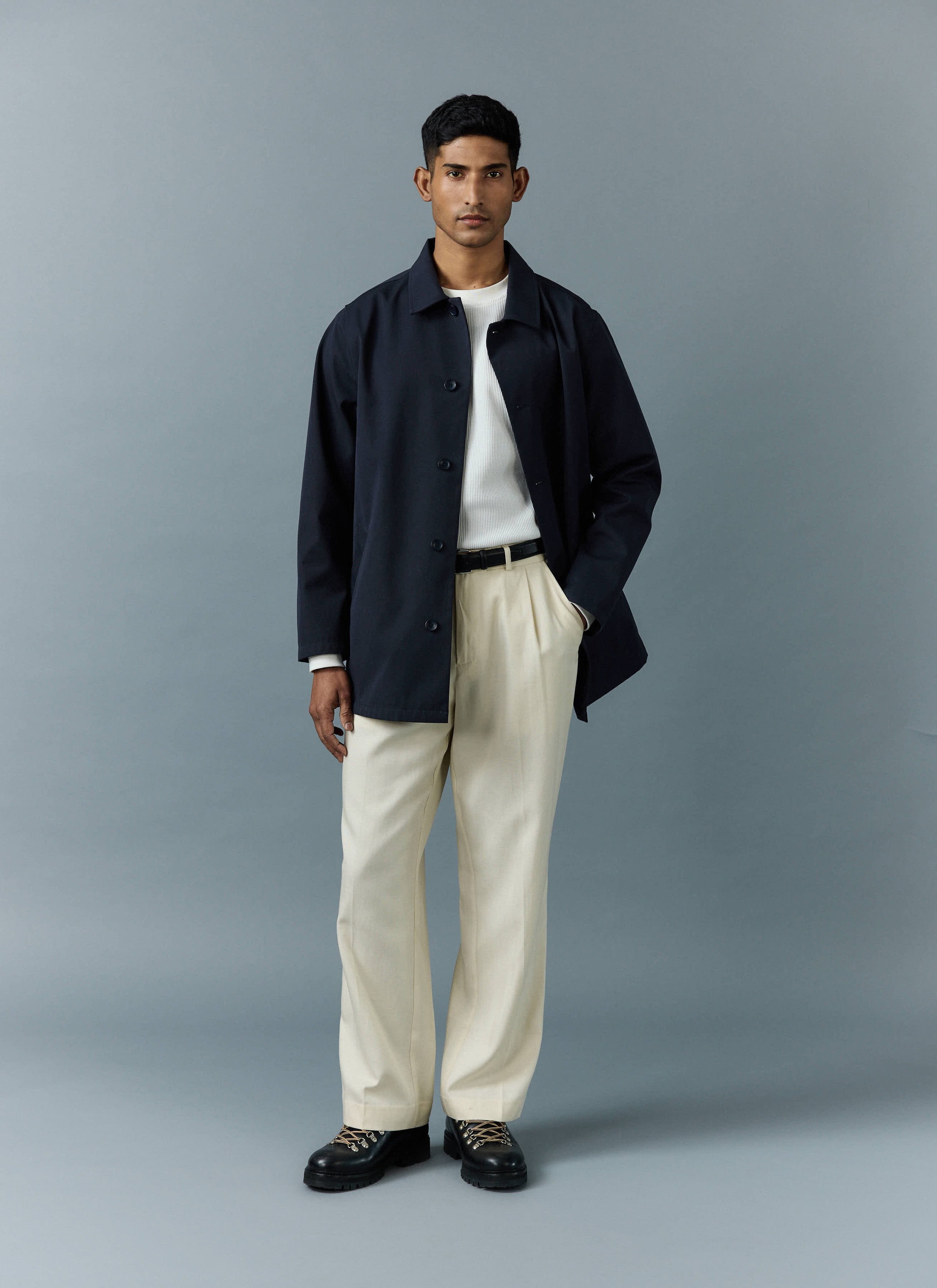 A model wears the Percival Sherlock Short Trench Coat in navy, styled with a white top and cream trousers.