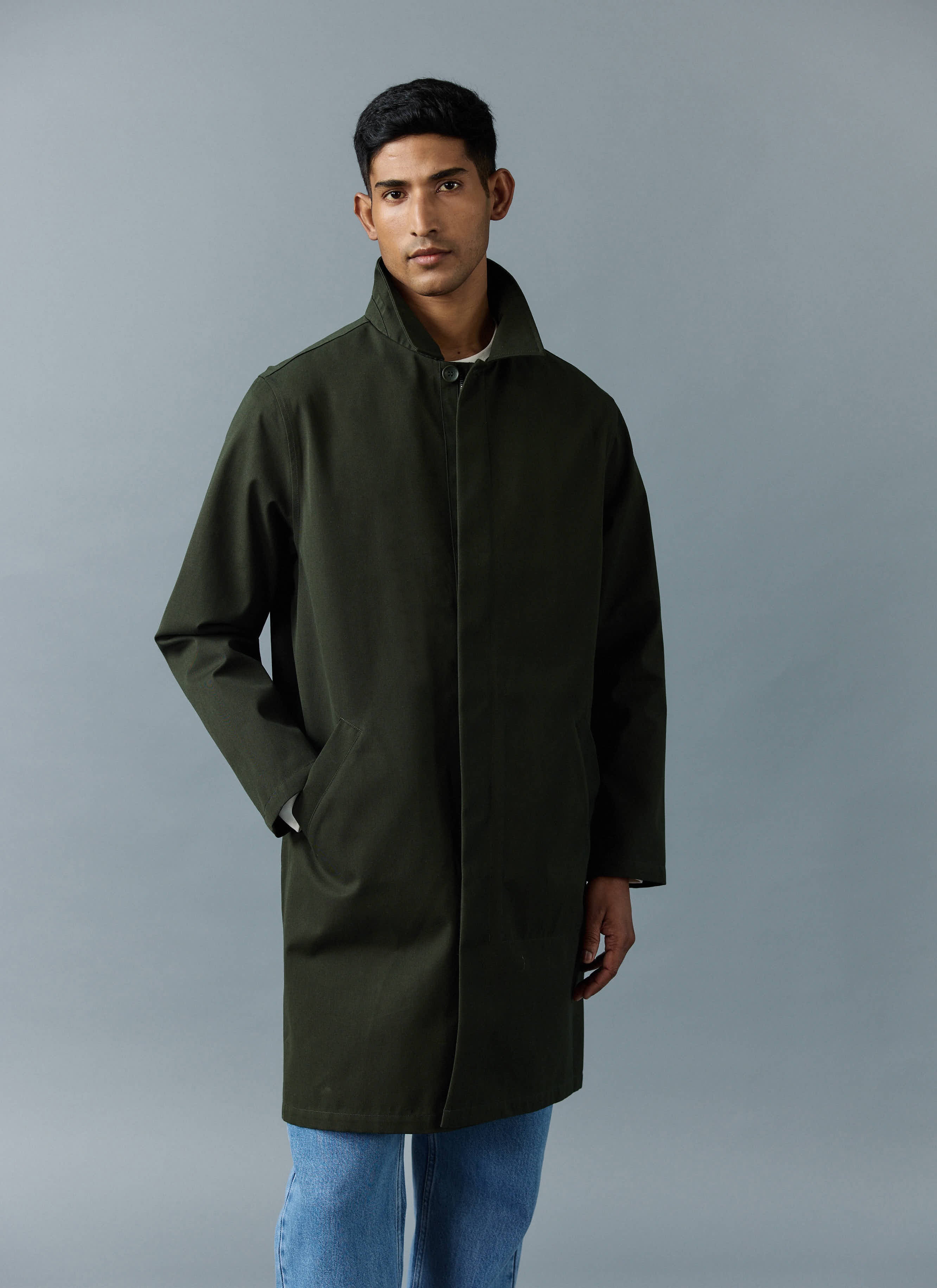 A model wears the Percival Greyson Long Trench Coat in Forest Green over a white t-shirt and blue jeans.