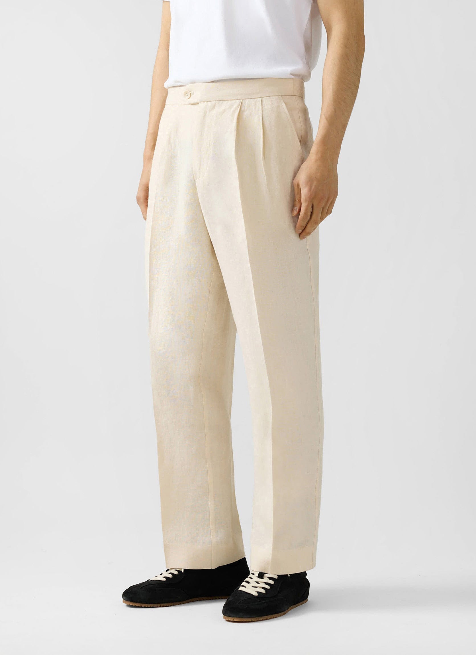 Percival cream linen pleated trousers in a relaxed fit, styled with a white t-shirt and black trainers.