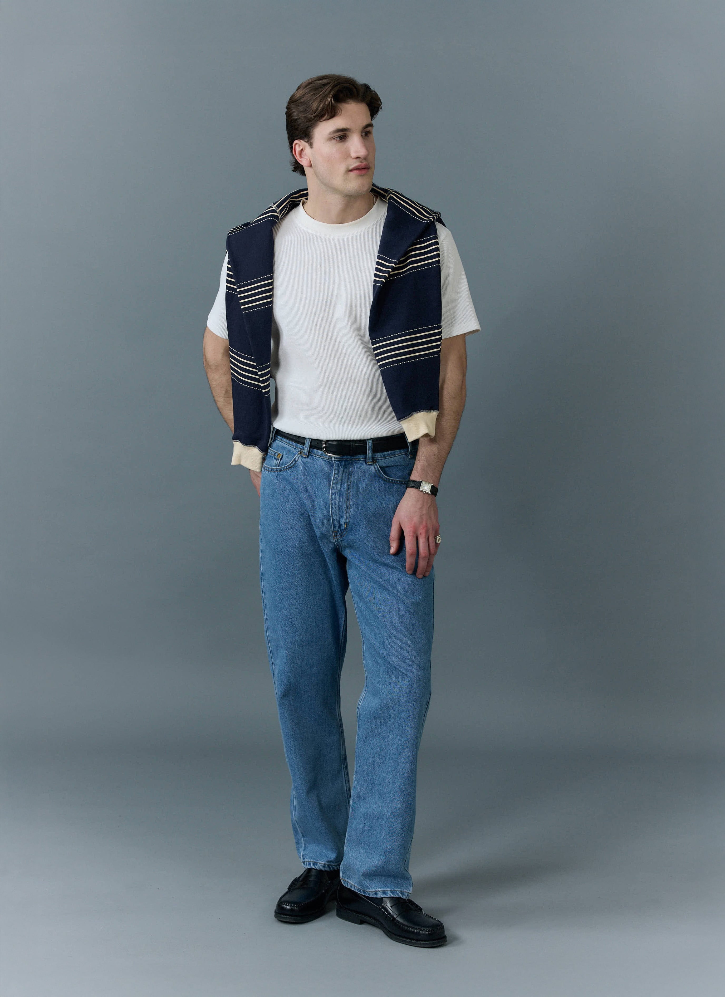 A male model wears Percival's light wash blue straight leg denim jeans with a white t-shirt and a navy striped jumper.