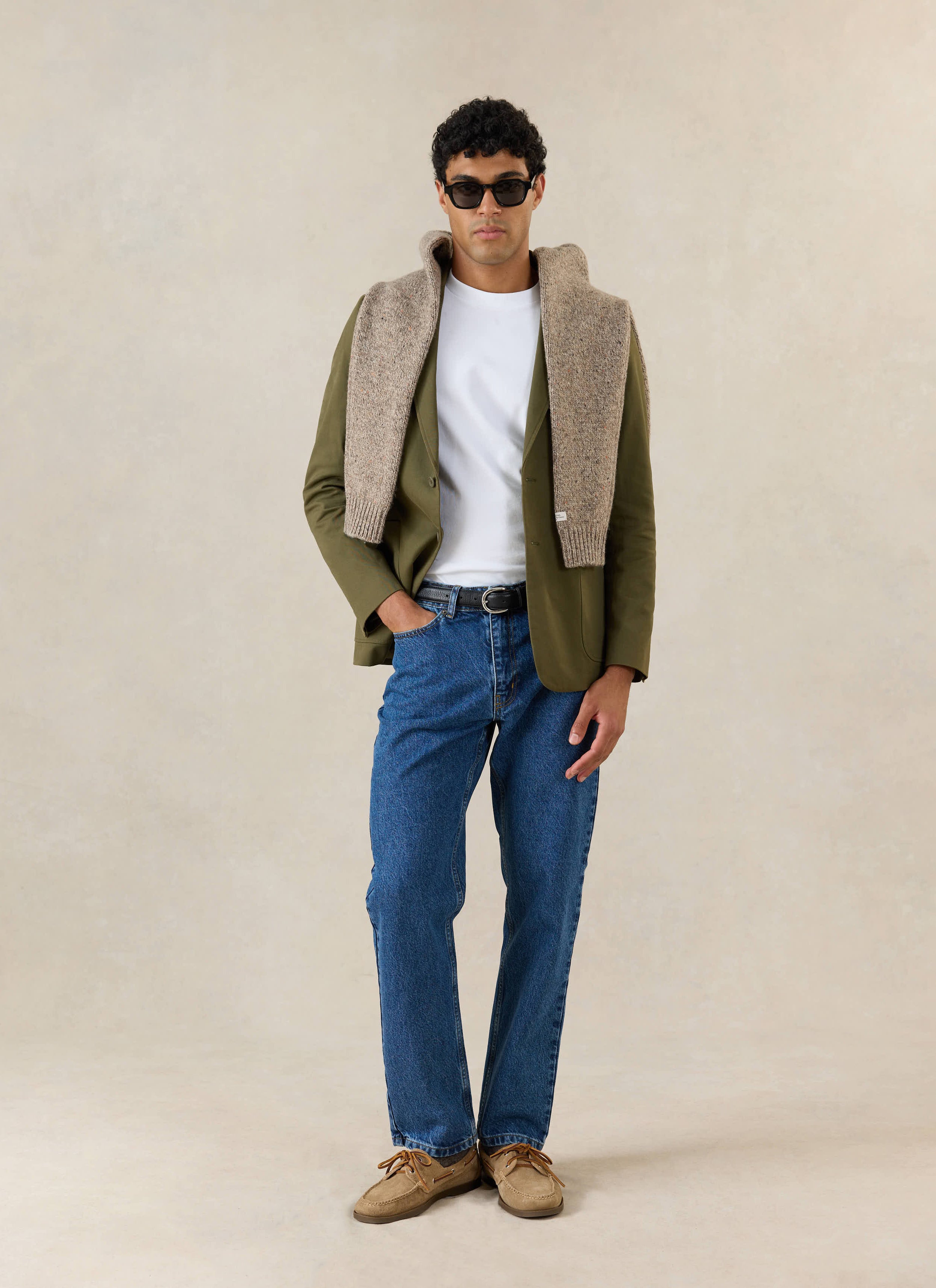 A model wears the Percival Tailored Blazer in Forest Brushed Moleskin, styled with blue jeans and a tan knit over shoulders.