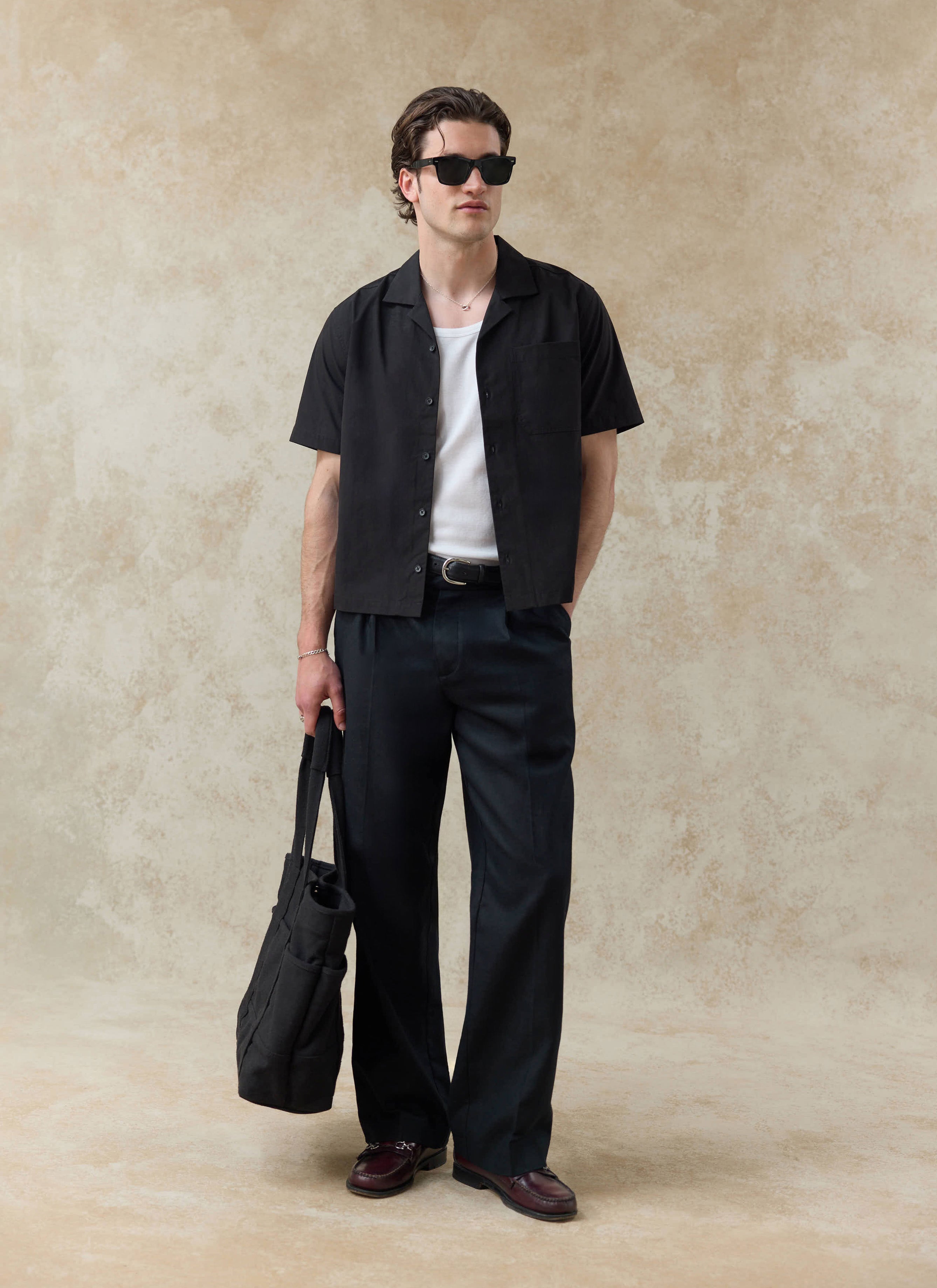 Percival black cotton Daniel Boxy Cuban Shirt worn open with a white vest and dark trousers in a studio setting.