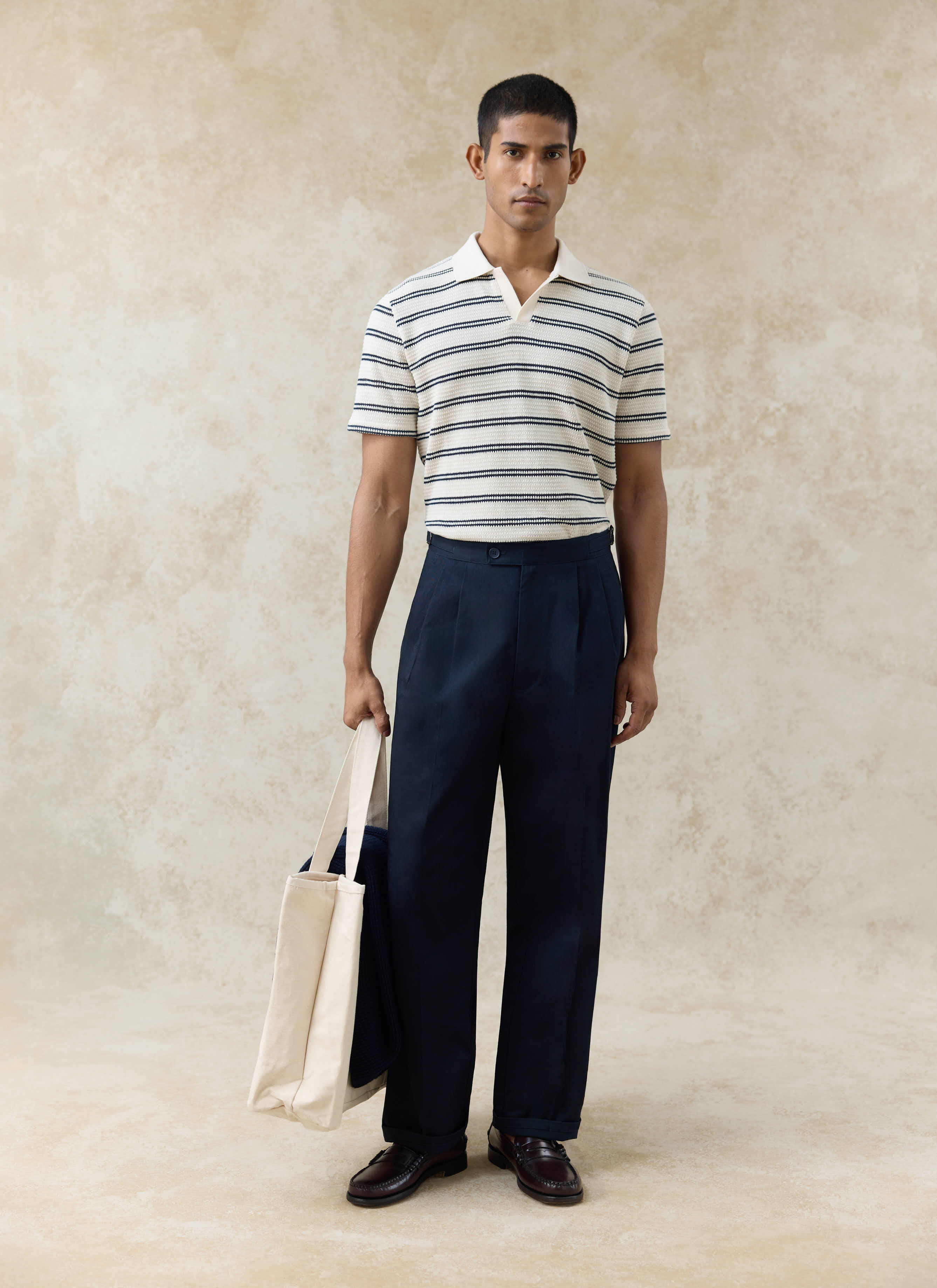 Percival Moore Polo in cream textured cotton with black stripes, paired with navy trousers and a canvas tote bag.