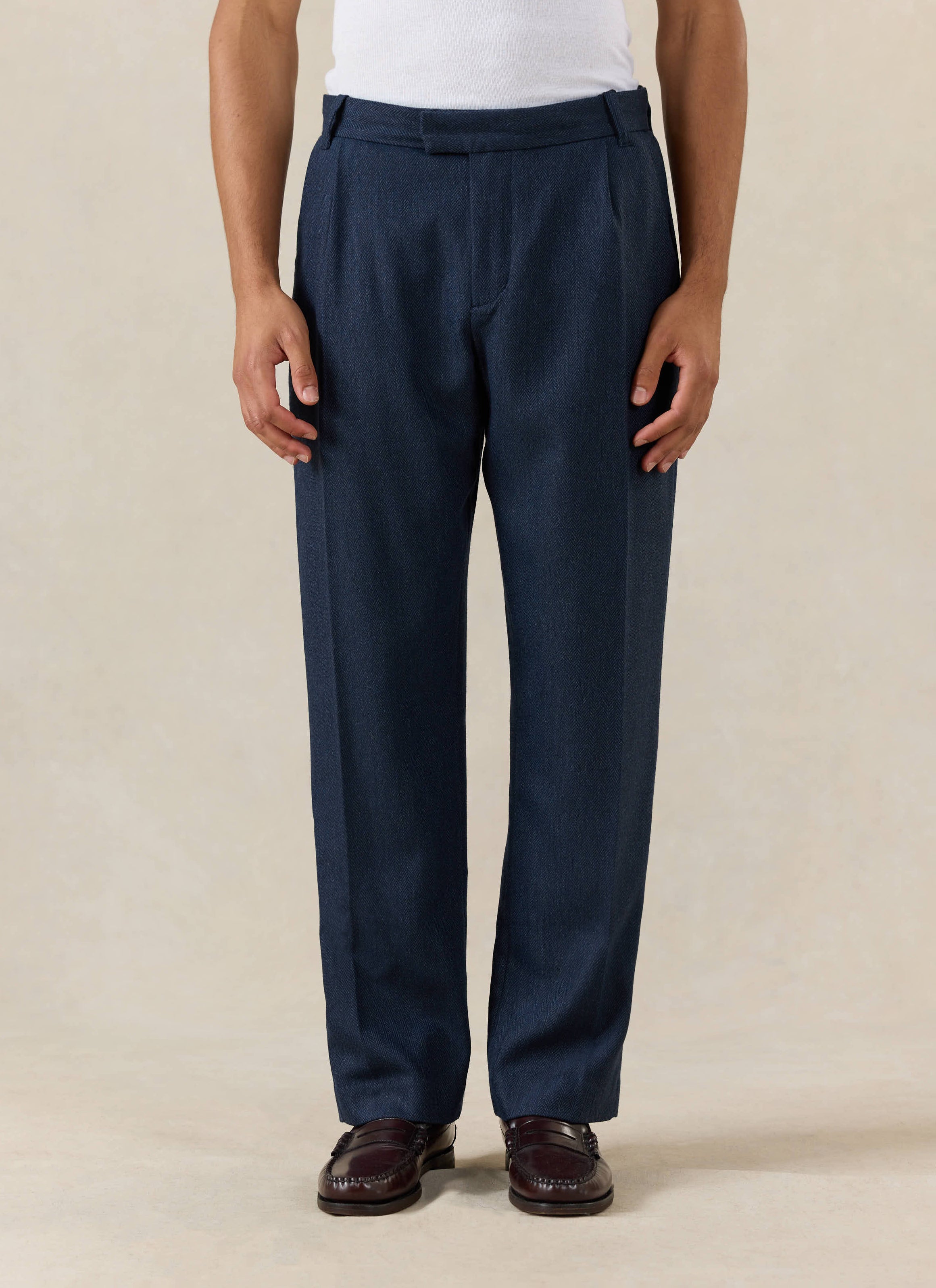 Percival Stanley Pleated Tailored Trousers in Navy Herringbone Wool, worn with a white t-shirt and dark brown loafers.