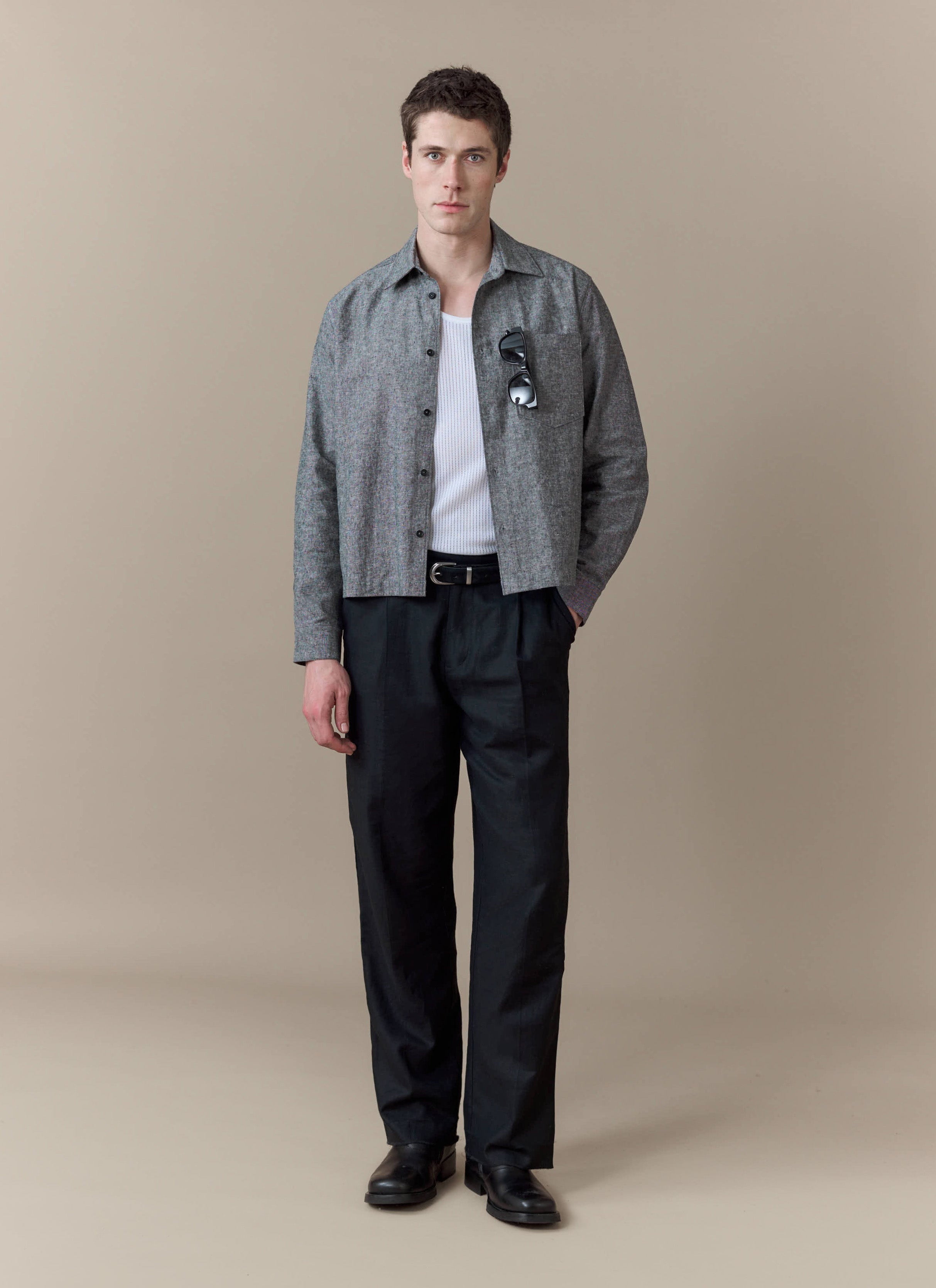 A model wears the grey Textured Boxy Shirt from Percival, styled with a white vest and smart black trousers.