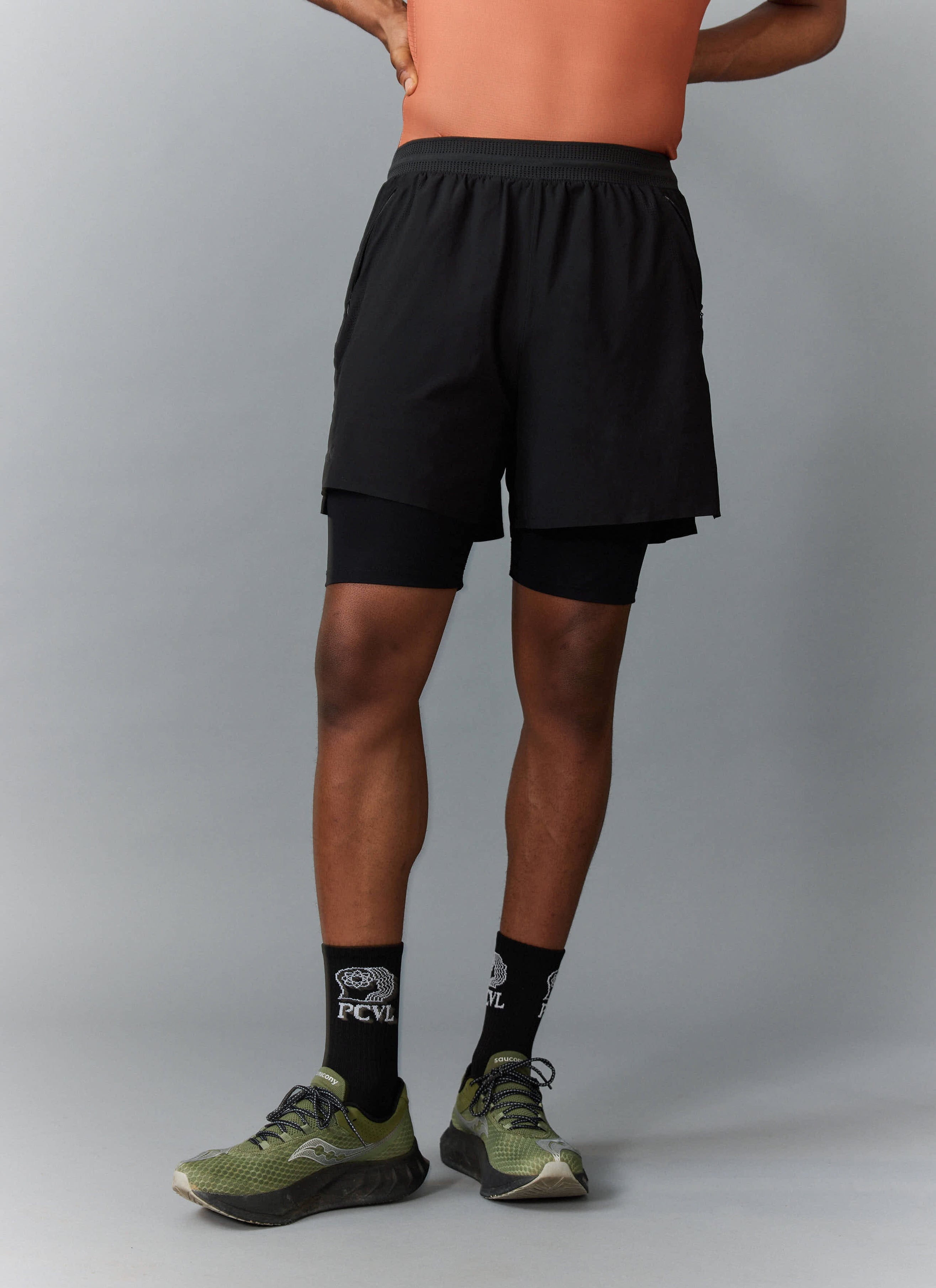 Back view of a model wearing the Percival PCVL 2 in 1 Shorts in black, with matching PCVL socks and khaki trainers.