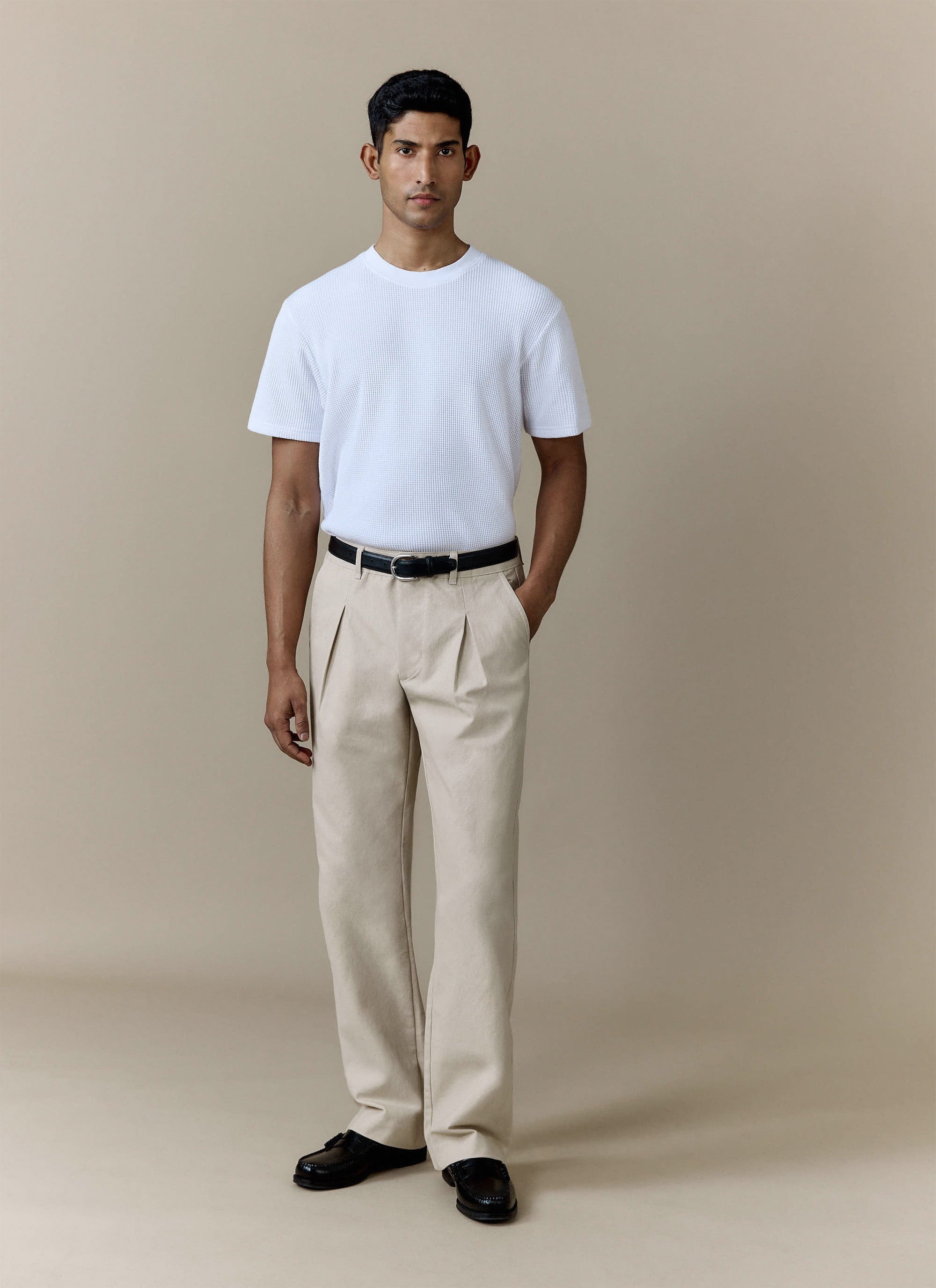A model wears the ecru Seb Inverted Pleat Trousers from Percival, styled with a white t-shirt and black loafers.