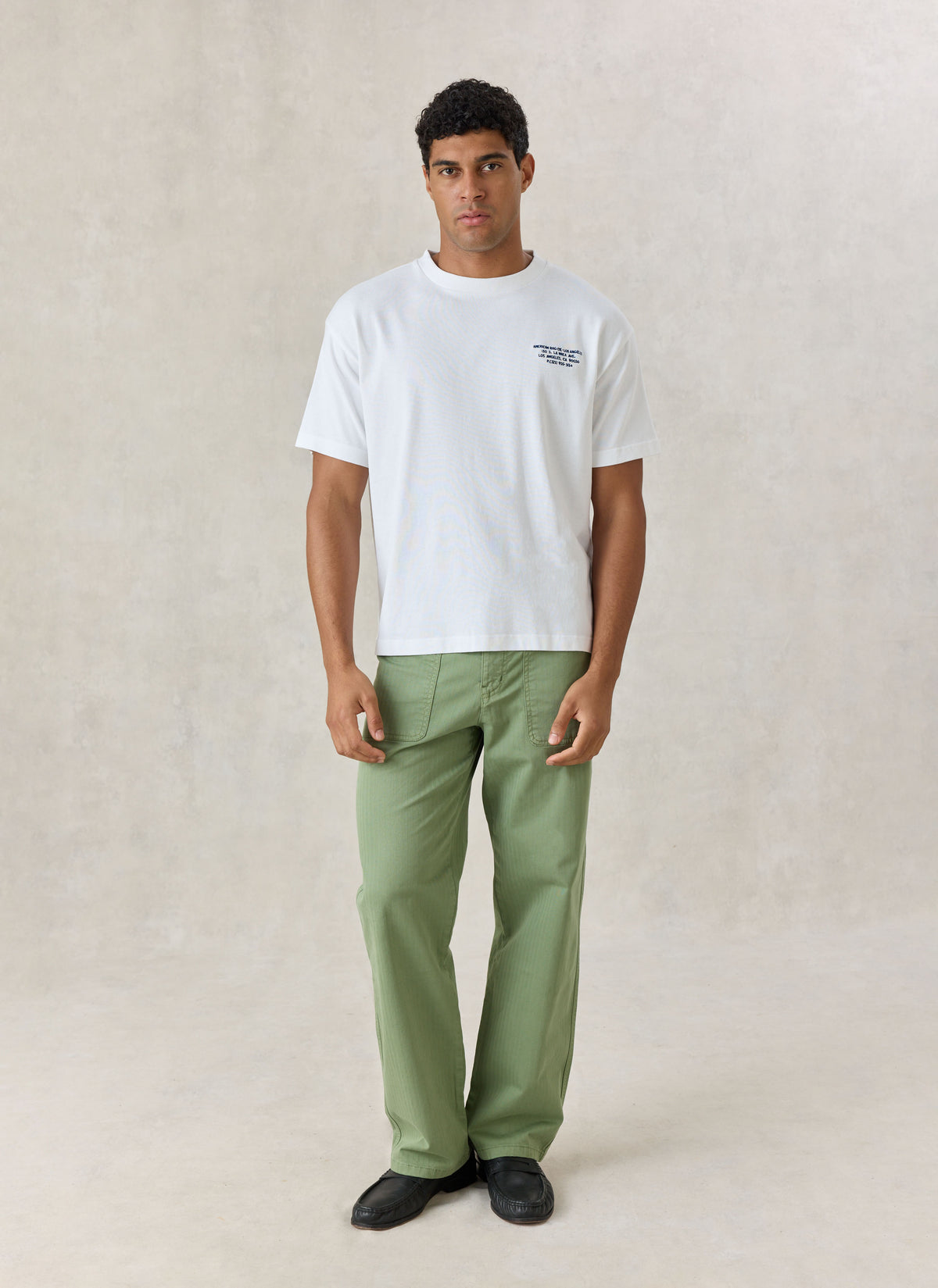 A model wearing the white American Rag x Percival organic cotton oversized t-shirt with green trousers.