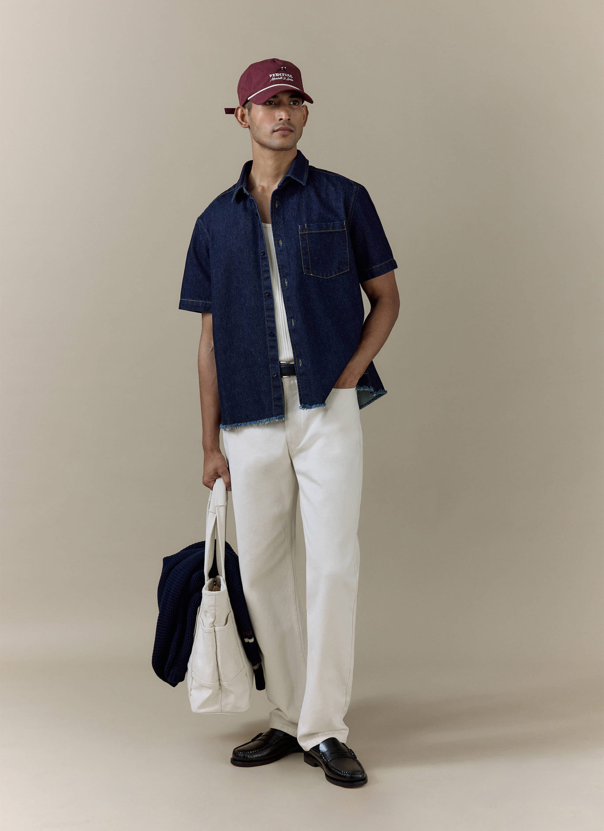 Percival Harley Denim Cropped Boxy Shirt in dark indigo cotton, styled with white trousers and a burgundy cap.