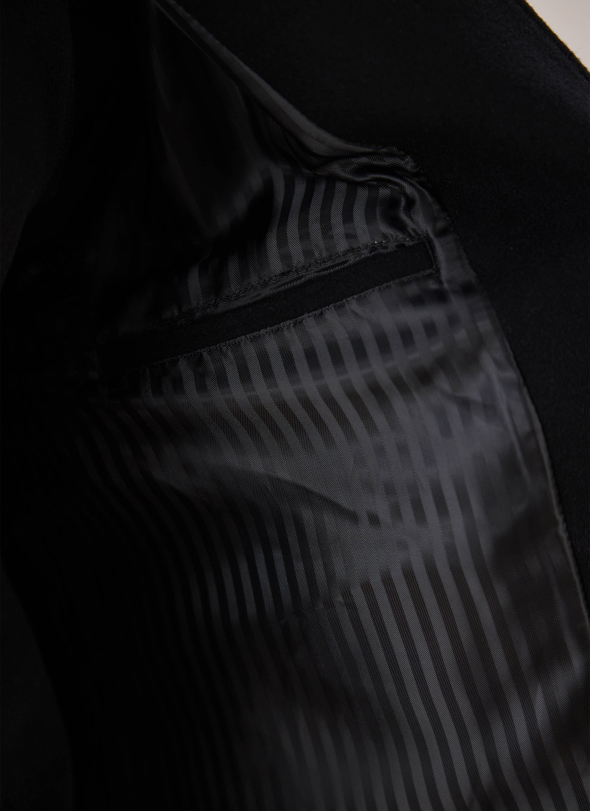 A close-up of the interior striped lining and pocket of the black Melton wool peacoat from Percival.