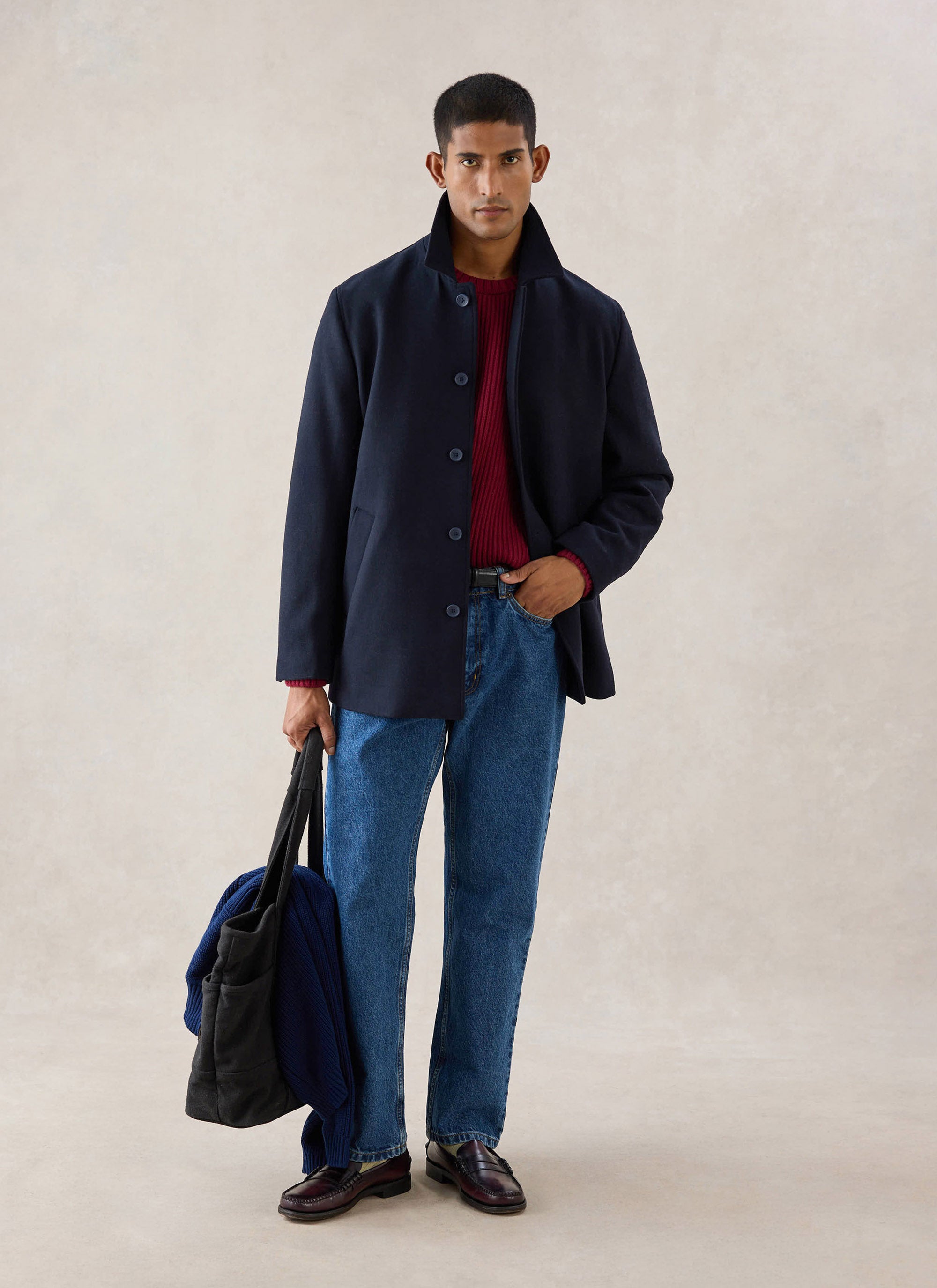 A model wearing the navy Percival wool blend pea coat over a red knitwear jumper, blue jeans and holding a dark bag.