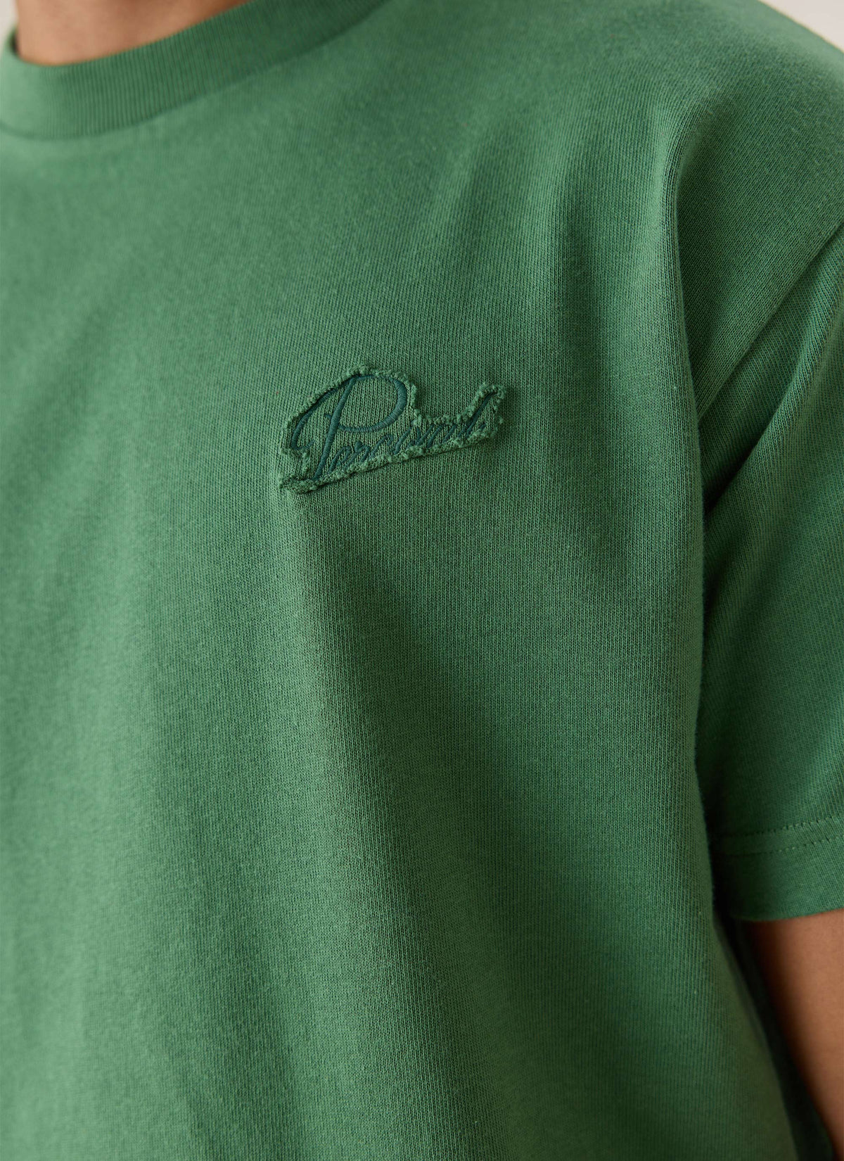 A close-up of the Percival forest green organic cotton oversized T-shirt showing the tonal script appliqué on the chest.