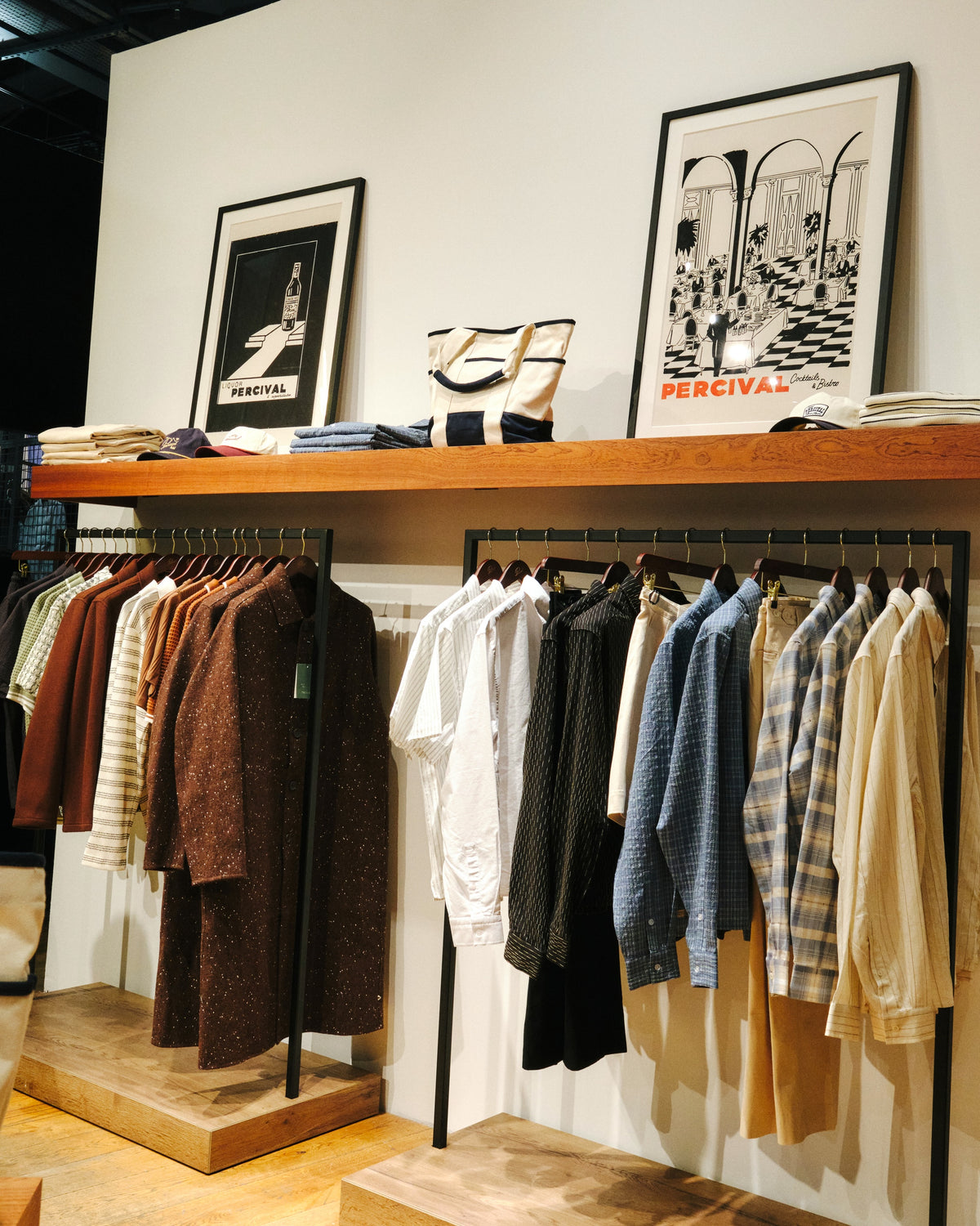 A Percival store display featuring shirts below a wooden shelf showcasing framed Percival prints and accessories.