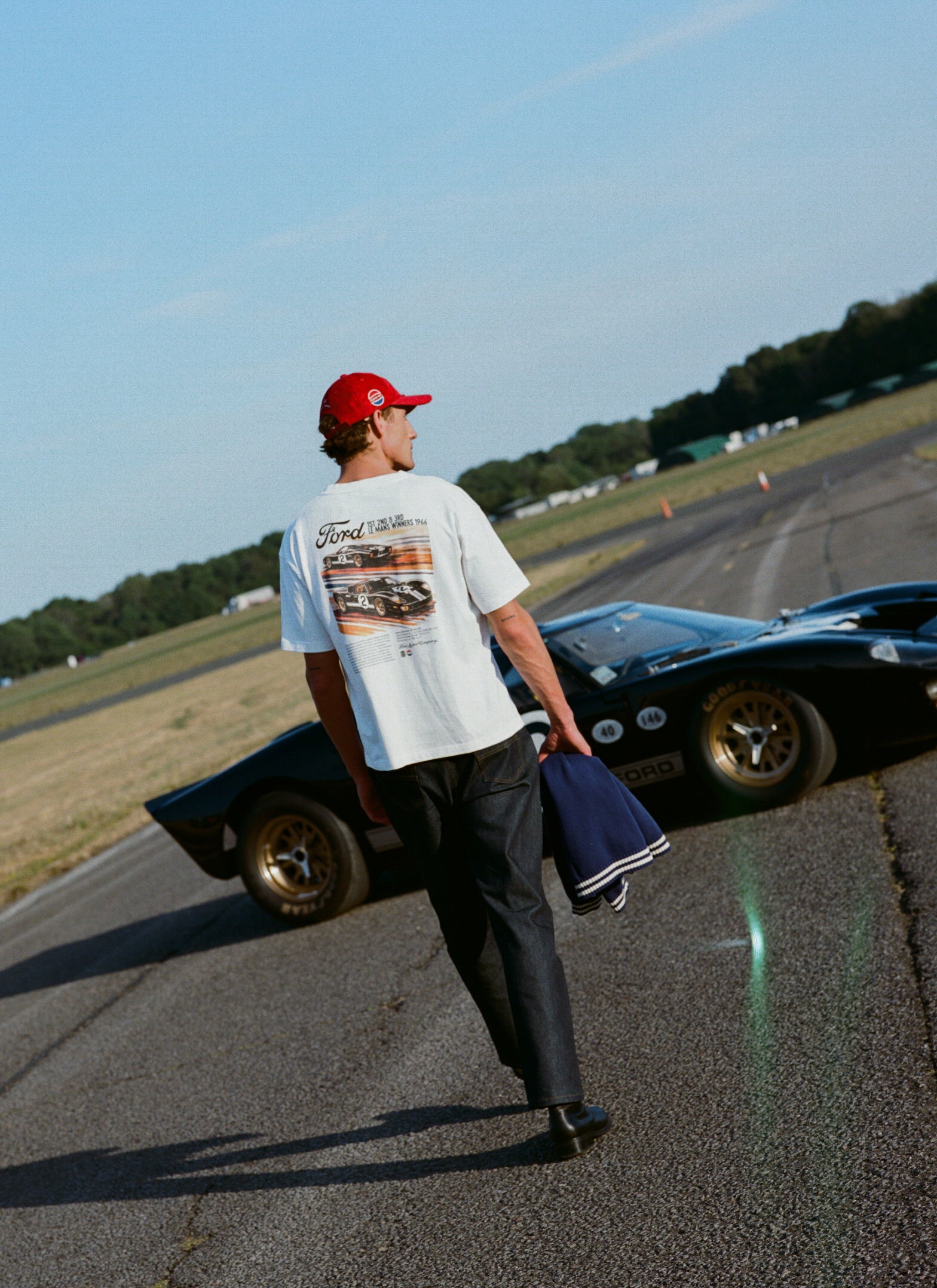 White Percival x Ford Le Mans oversized t-shirt with a back graphic, styled with raw denim jeans on a racetrack.
