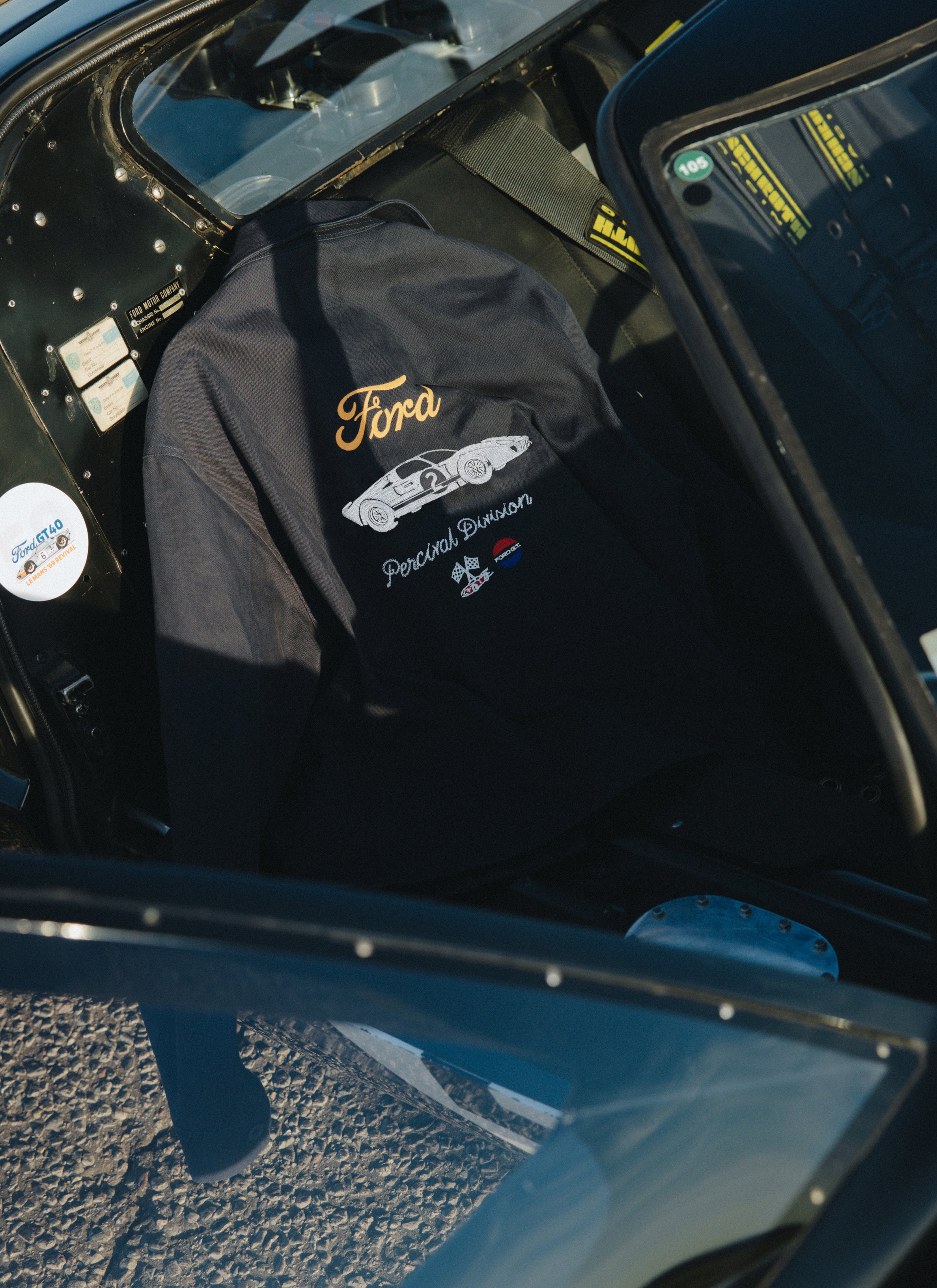 Navy Percival canvas jacket featuring Ford GT40 back embroidery, draped inside the cockpit of a vintage racing car.