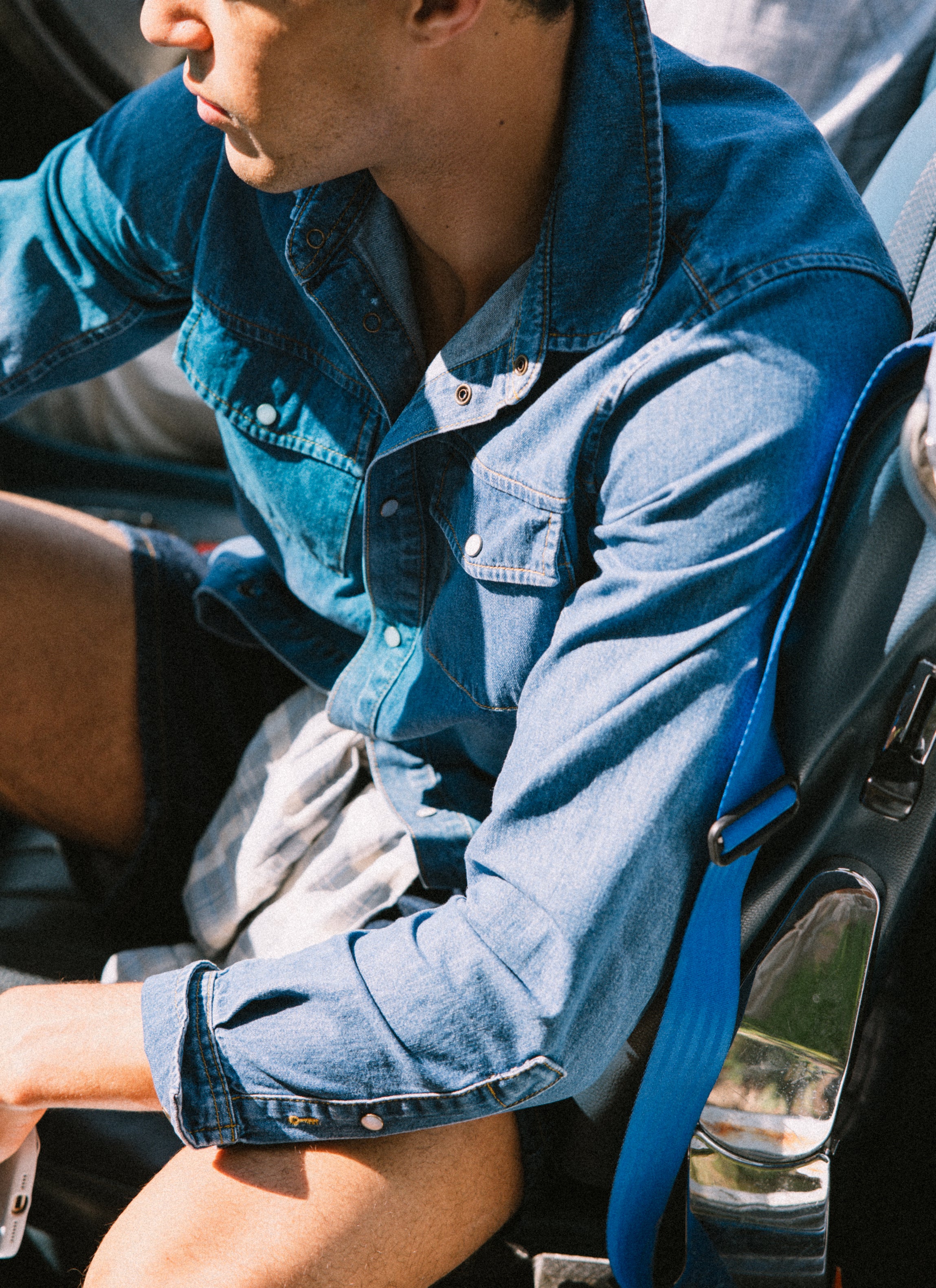 The Percival Vintage Wash Western Shirt in mid wash blue denim with pearl buttons, worn by a model sitting in a car.