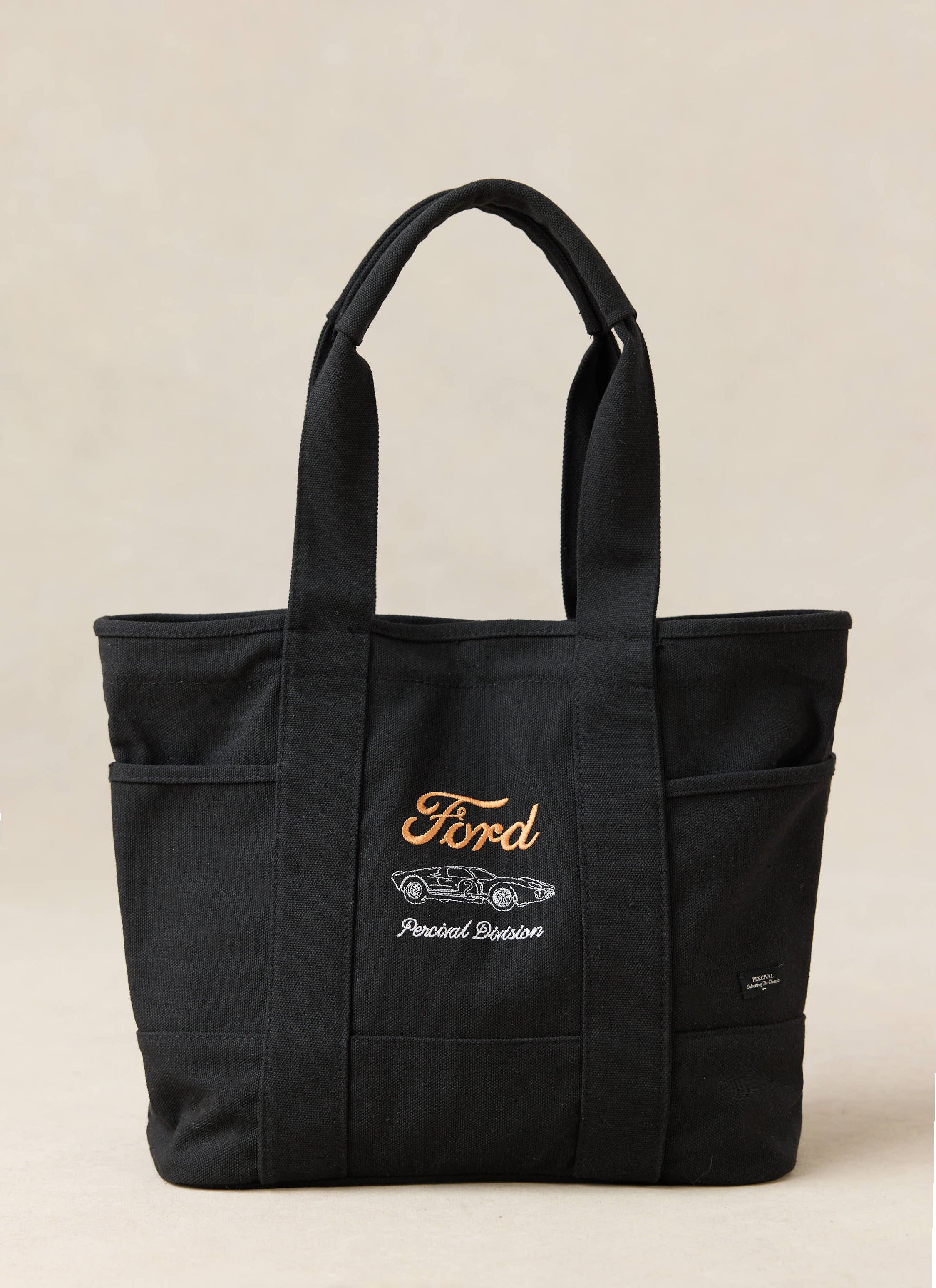Black canvas Ford x Percival tote bag featuring an embroidered GT40 graphic, orange branding, and side pockets.