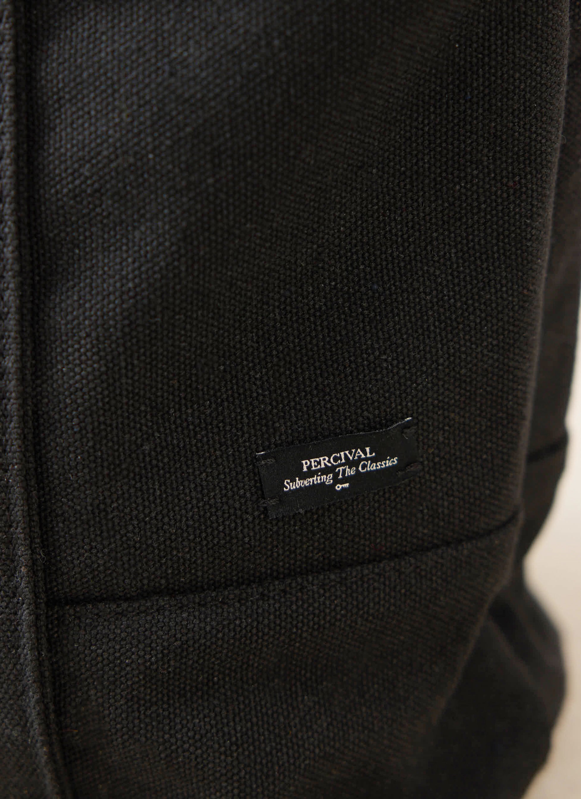 Woven Percival brand label on the black canvas material of a tote bag from the Ford x Percival GT40 collection.