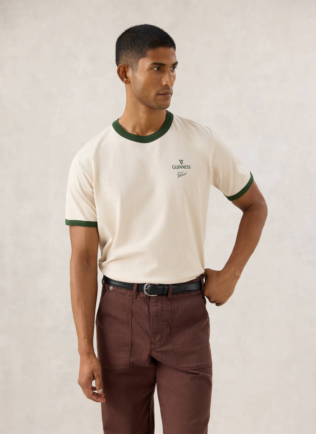 Model wearing the cream Guinness x Percival ringer T-shirt featuring forest green contrast trim and chest branding.
