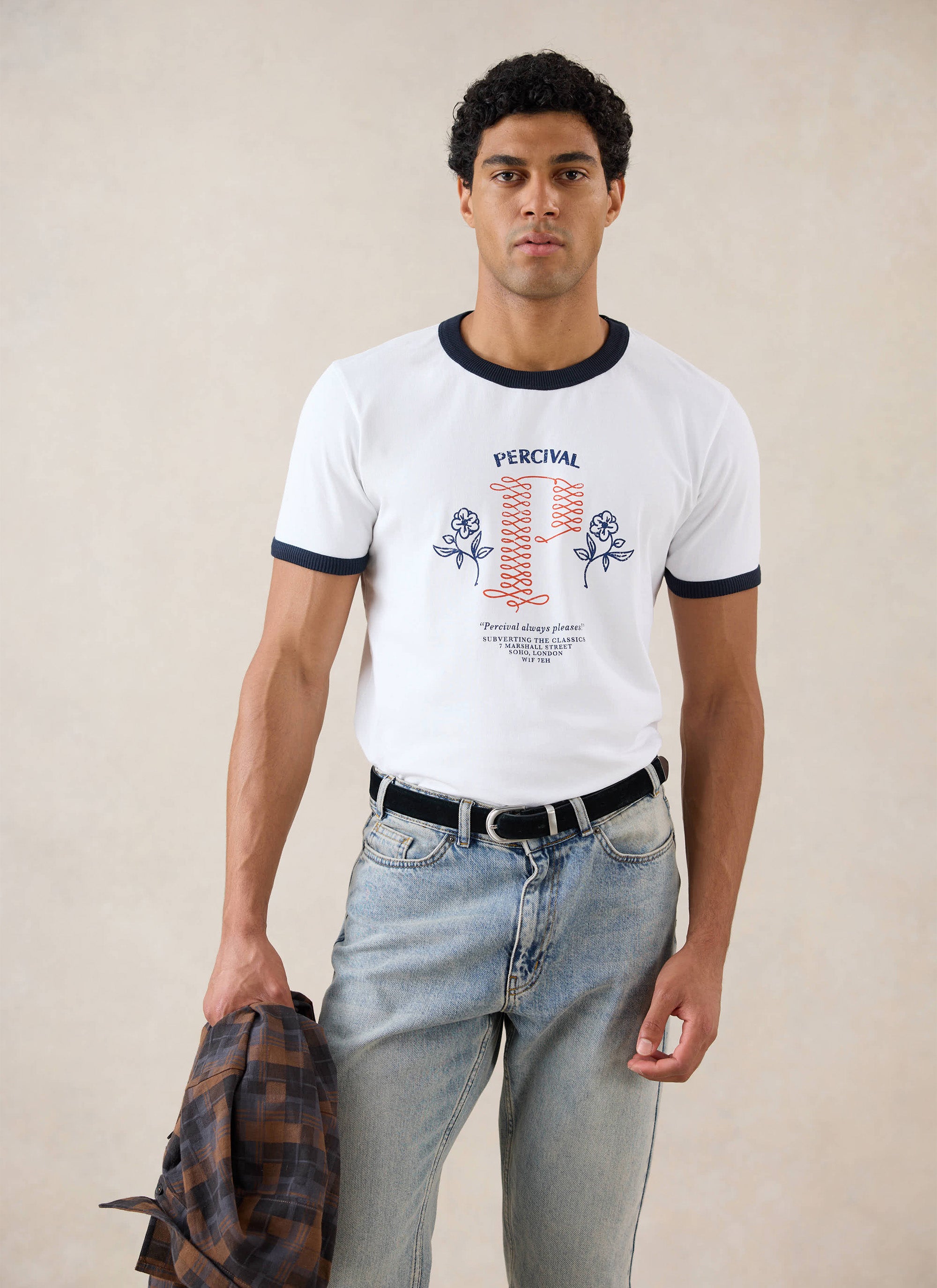 A model wears the white Tucker Ringer T-Shirt from Percival, featuring graphic embroidery, styled with light blue jeans.