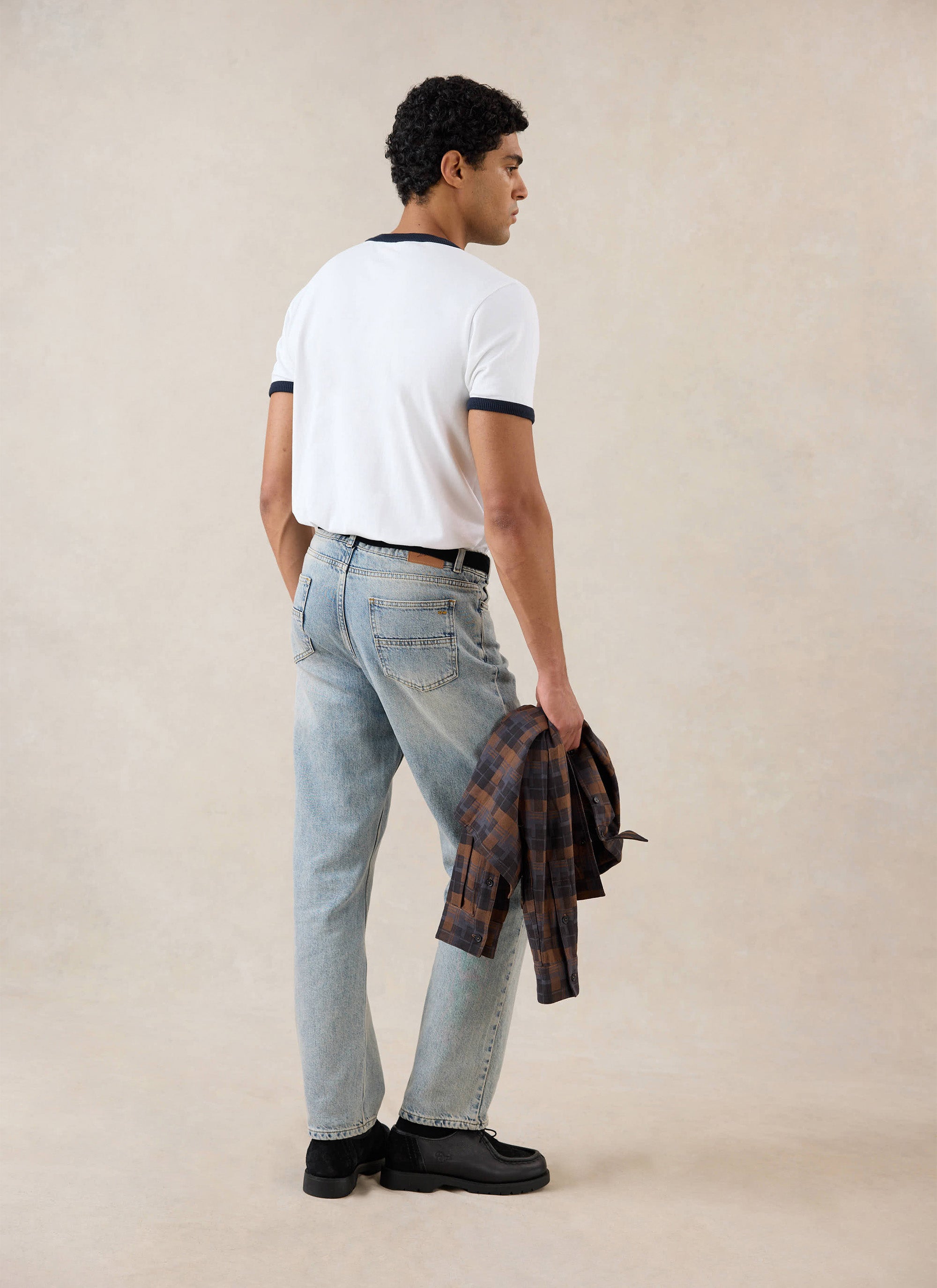 A model viewed from behind wears the white and navy Tucker Ringer T-Shirt from Percival, styled with light wash jeans.