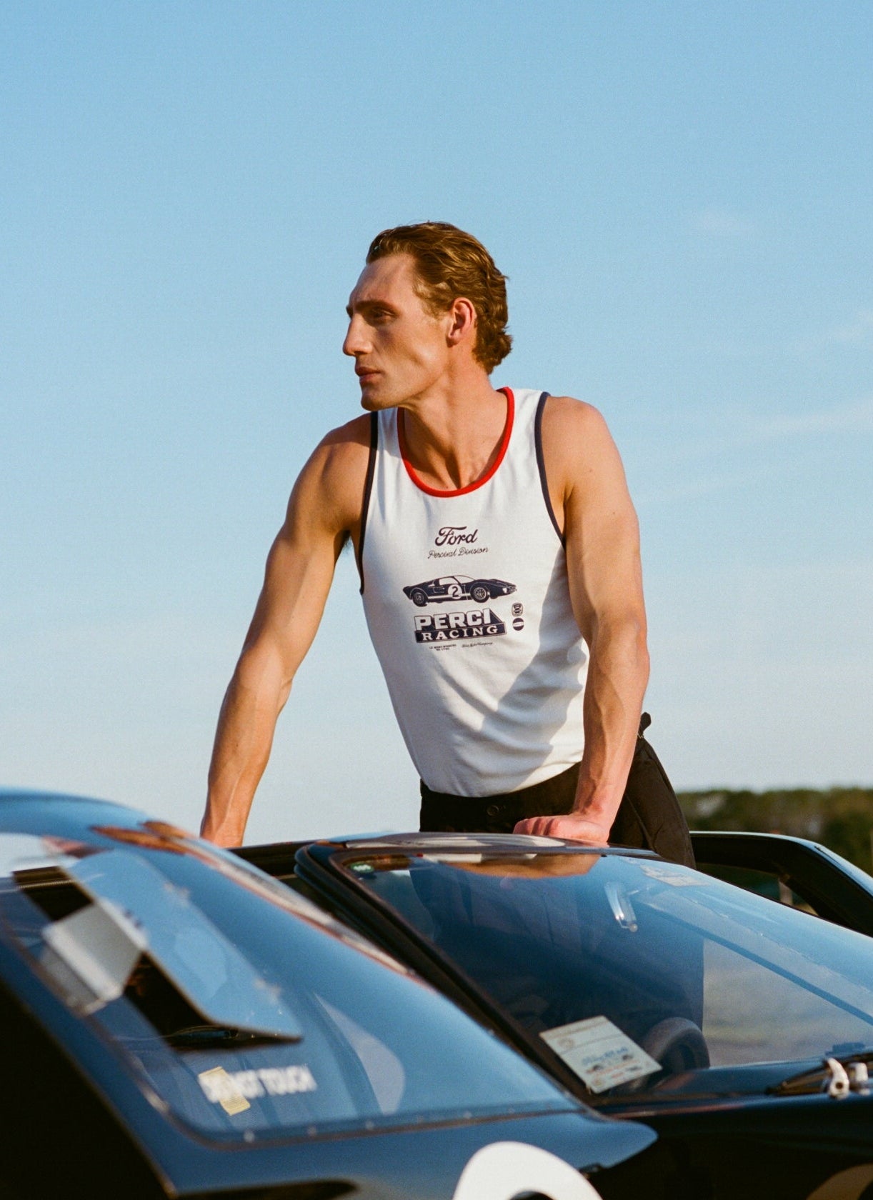 White Ford x Percival GT40 ringer vest with red and navy trim, worn by a model leaning on a vintage race car.