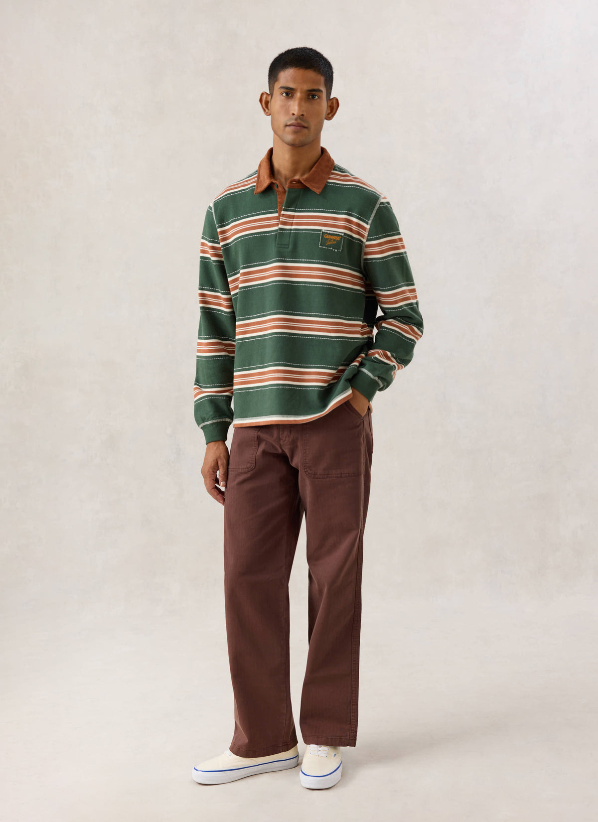 Model wearing the Guinness x Percival striped rugby polo in forest green, featuring a cord collar and chest patch.