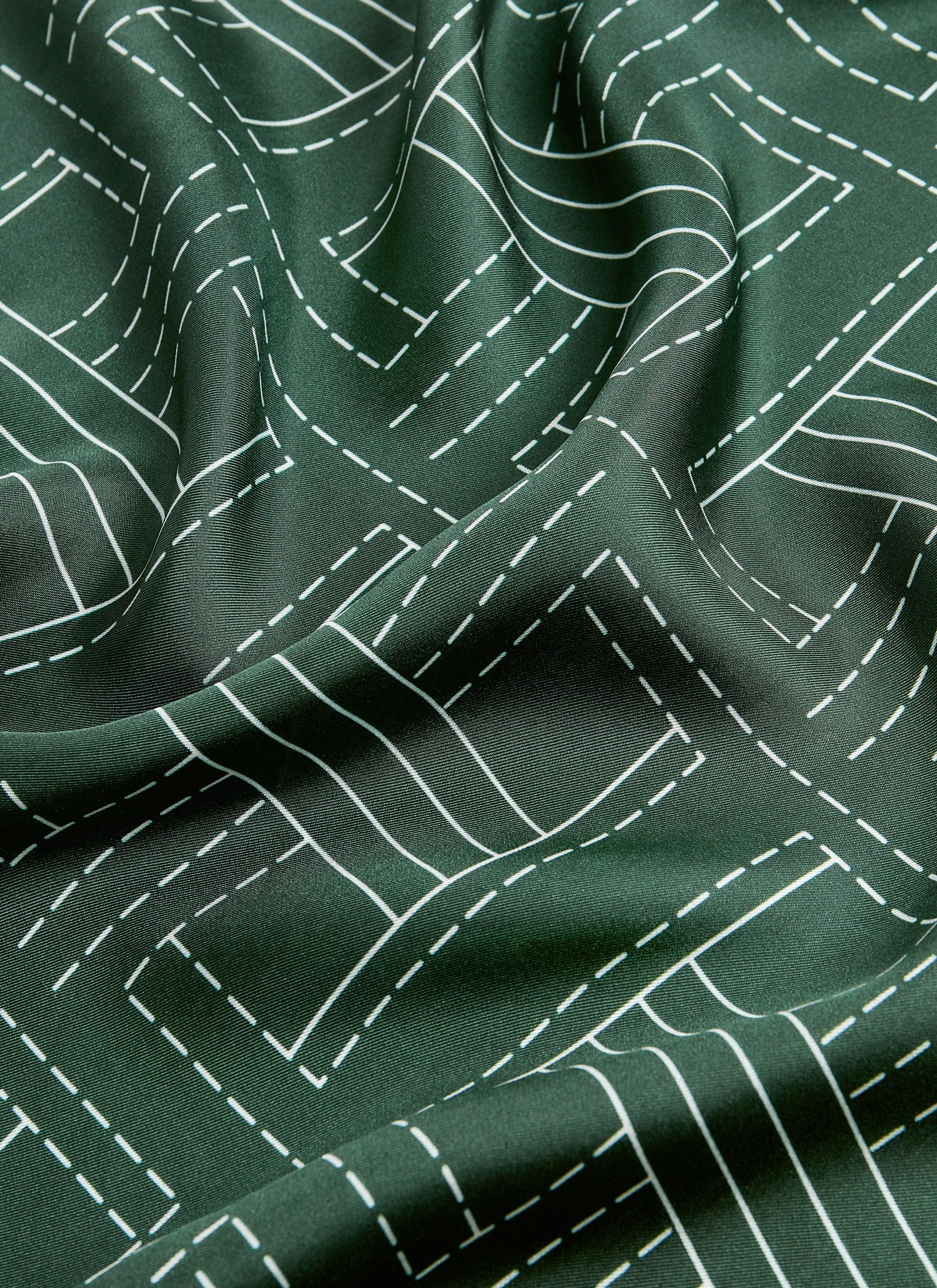 A close-up shot of the forest green silk fabric of the Sashiko Neckerchief by Percival, showing the white stitch pattern.