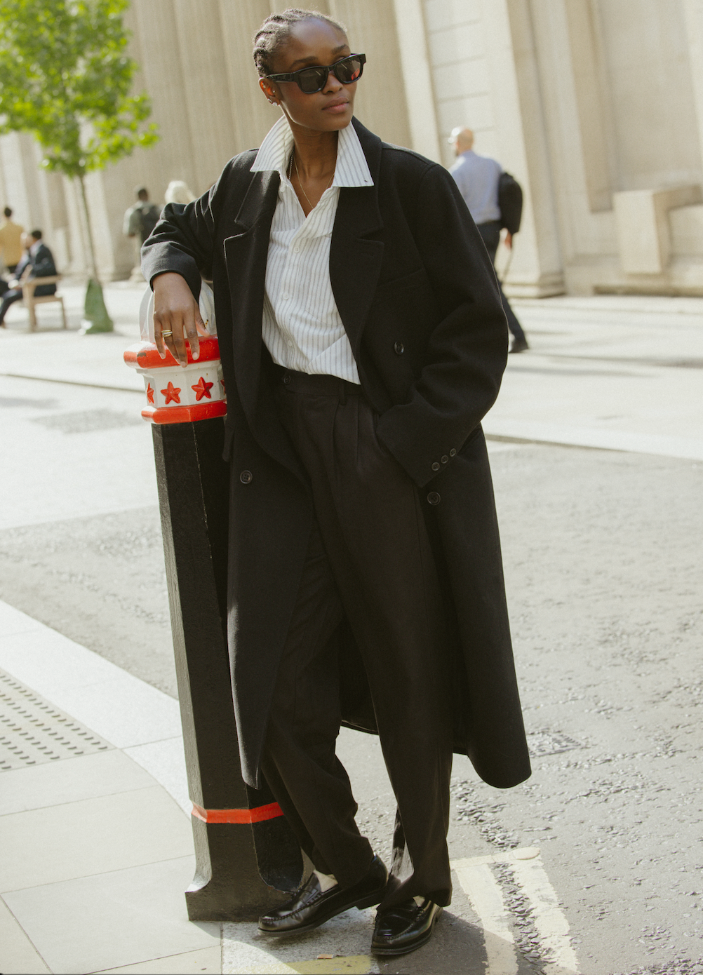 A model wearing the black Percival wool-blend double-breasted overcoat outdoors, paired with a striped shirt and trousers.
