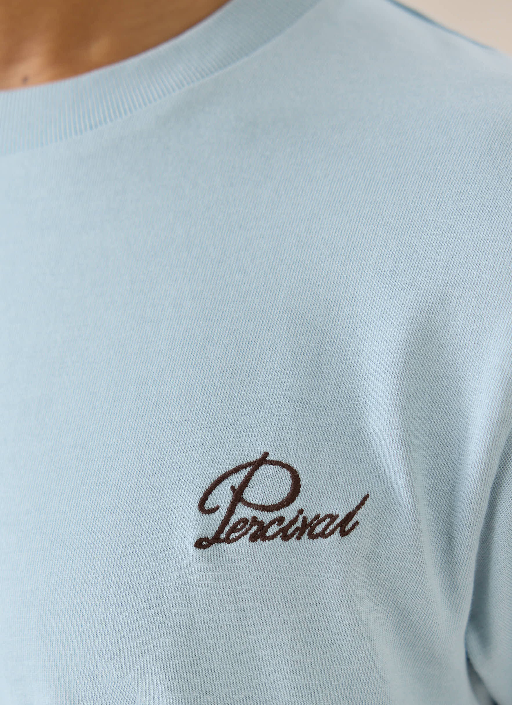 Light blue Percival organic cotton t-shirt featuring brown script embroidery detail on the chest.