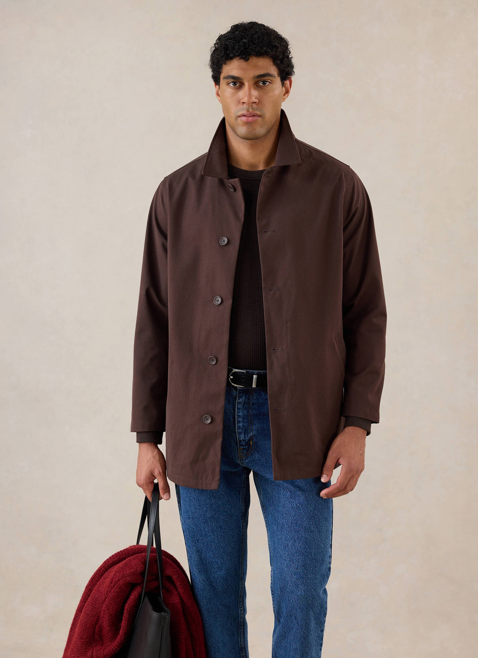 A model wears the Percival espresso brown Sherlock short trench coat over jeans, holding a bag.